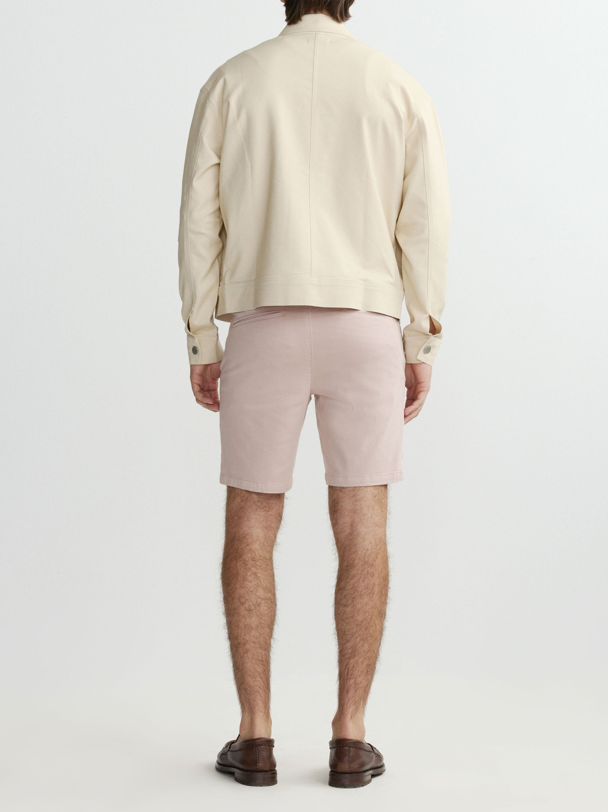 Person wearing a beige shirt and light pink shorts on a white background