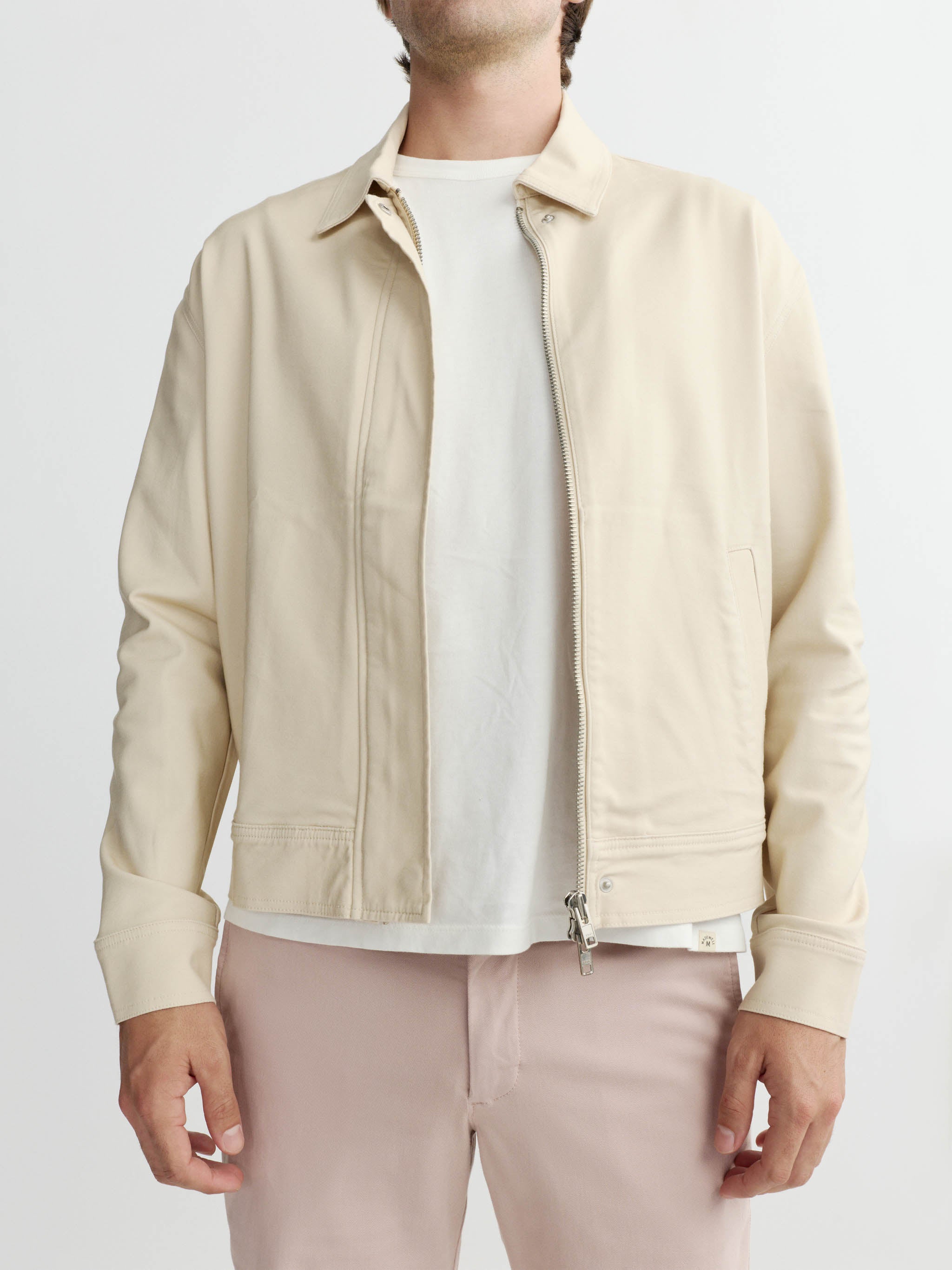 Man wearing a beige jacket over a white shirt on a light gray background