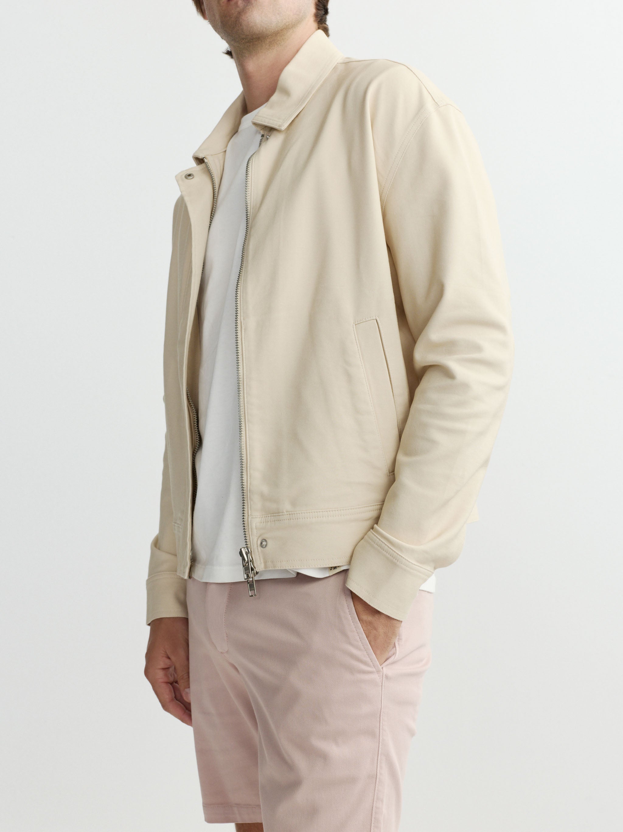 Person wearing a beige jacket and light pink shorts on a white background