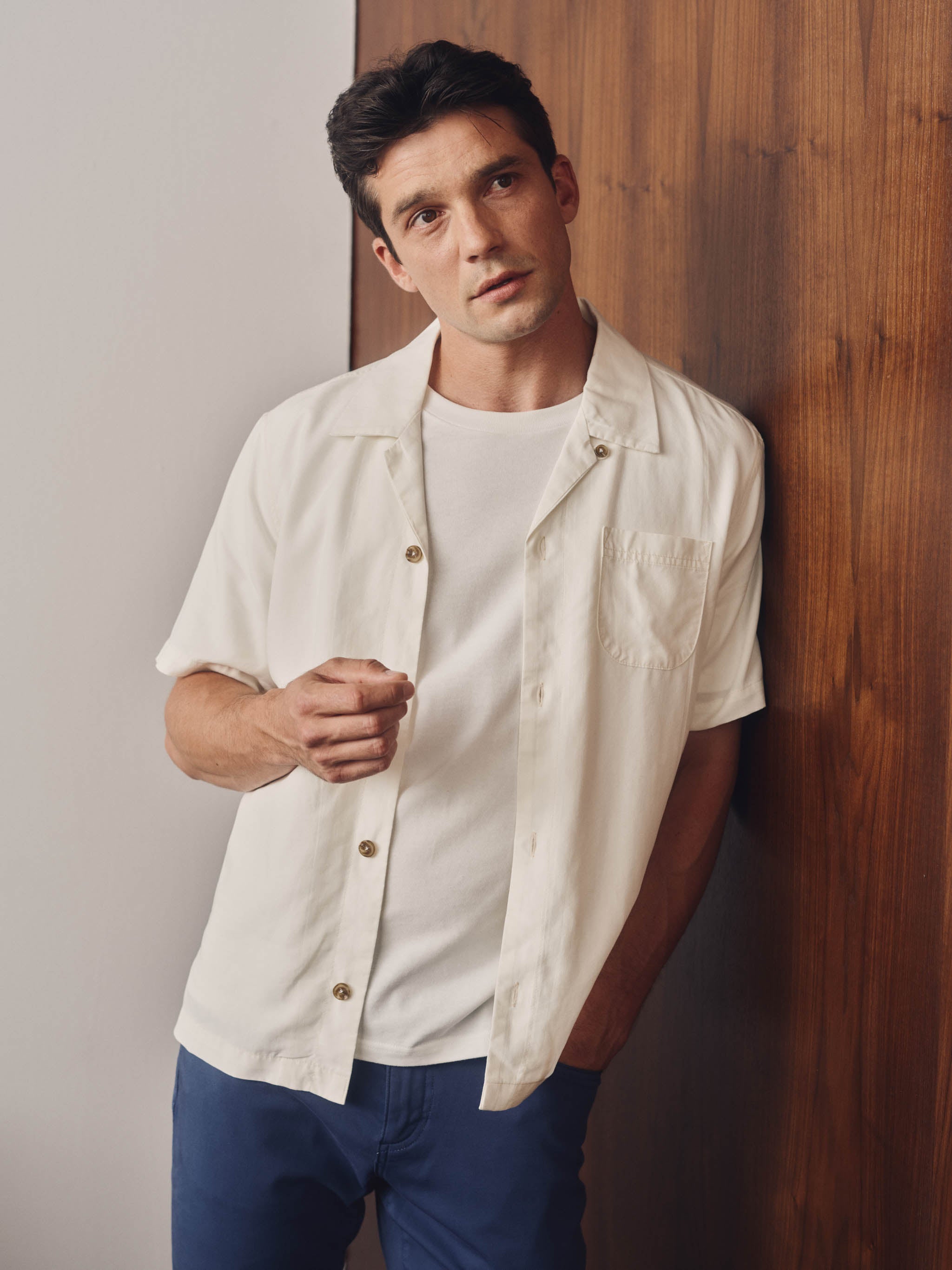 Person wearing a white short-sleeve shirt with gold buttons on a plain background