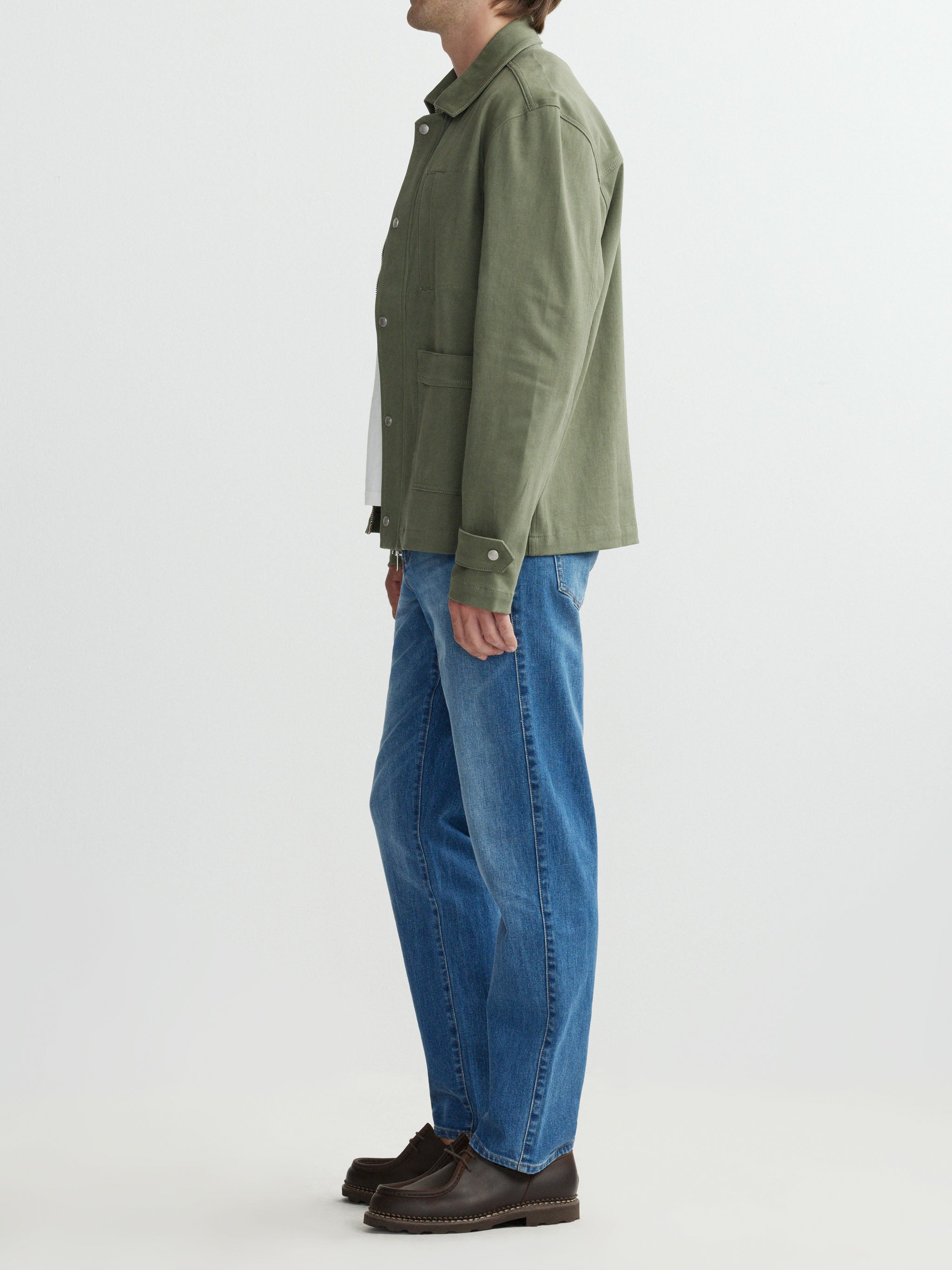 Person wearing a green jacket and blue jeans on a white background