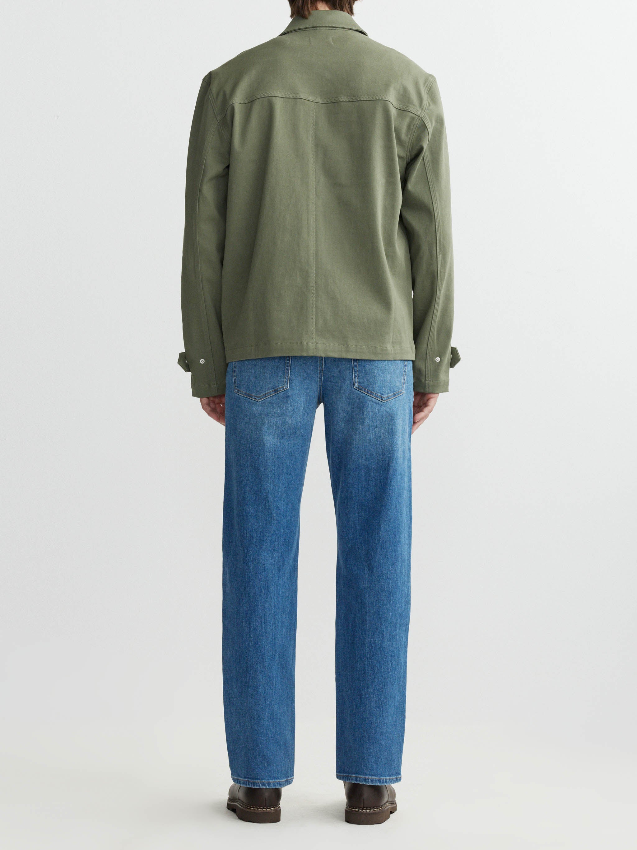 Person wearing a green jacket and blue jeans on a white background