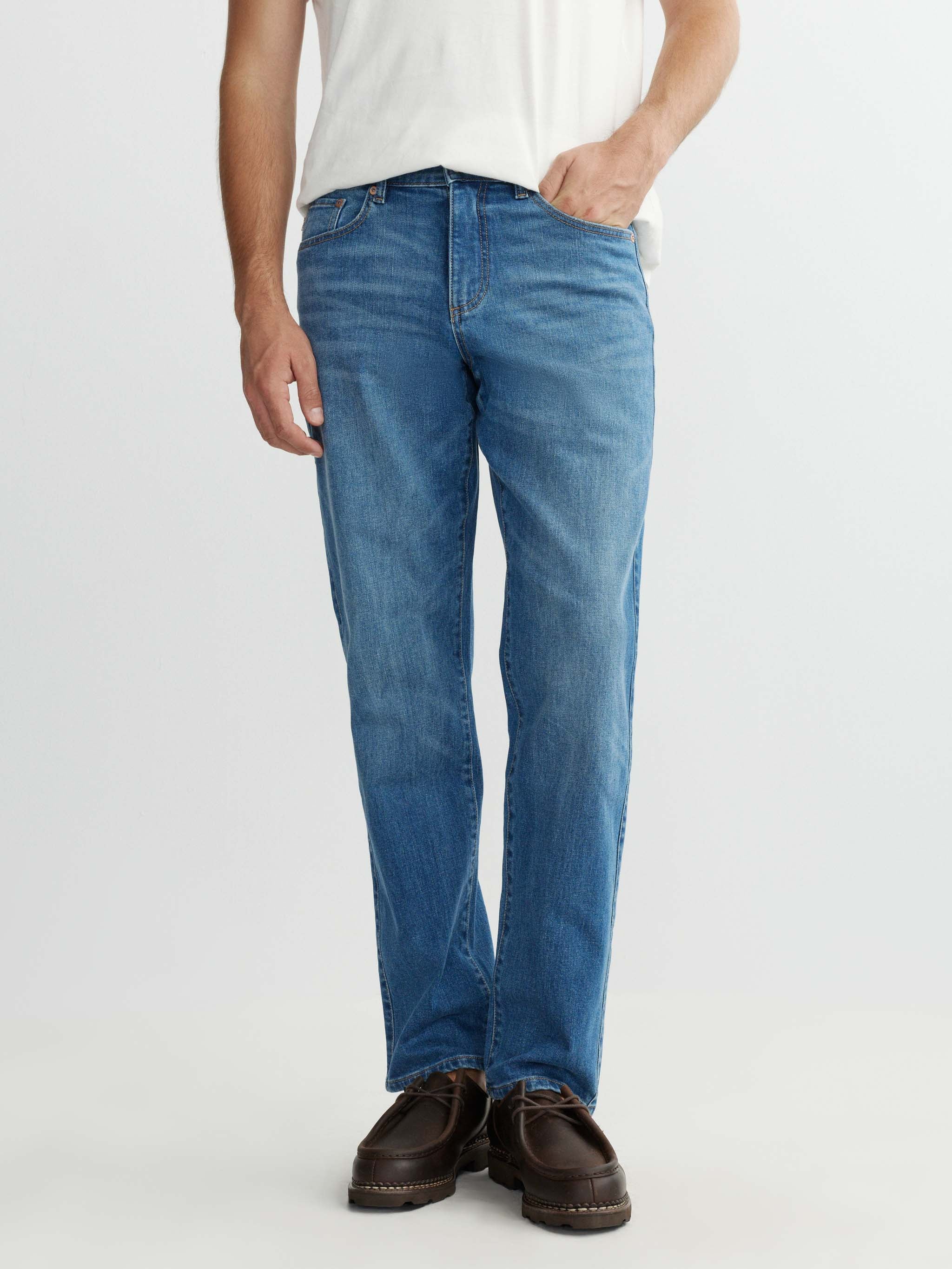 Person wearing blue jeans and brown shoes on a white background