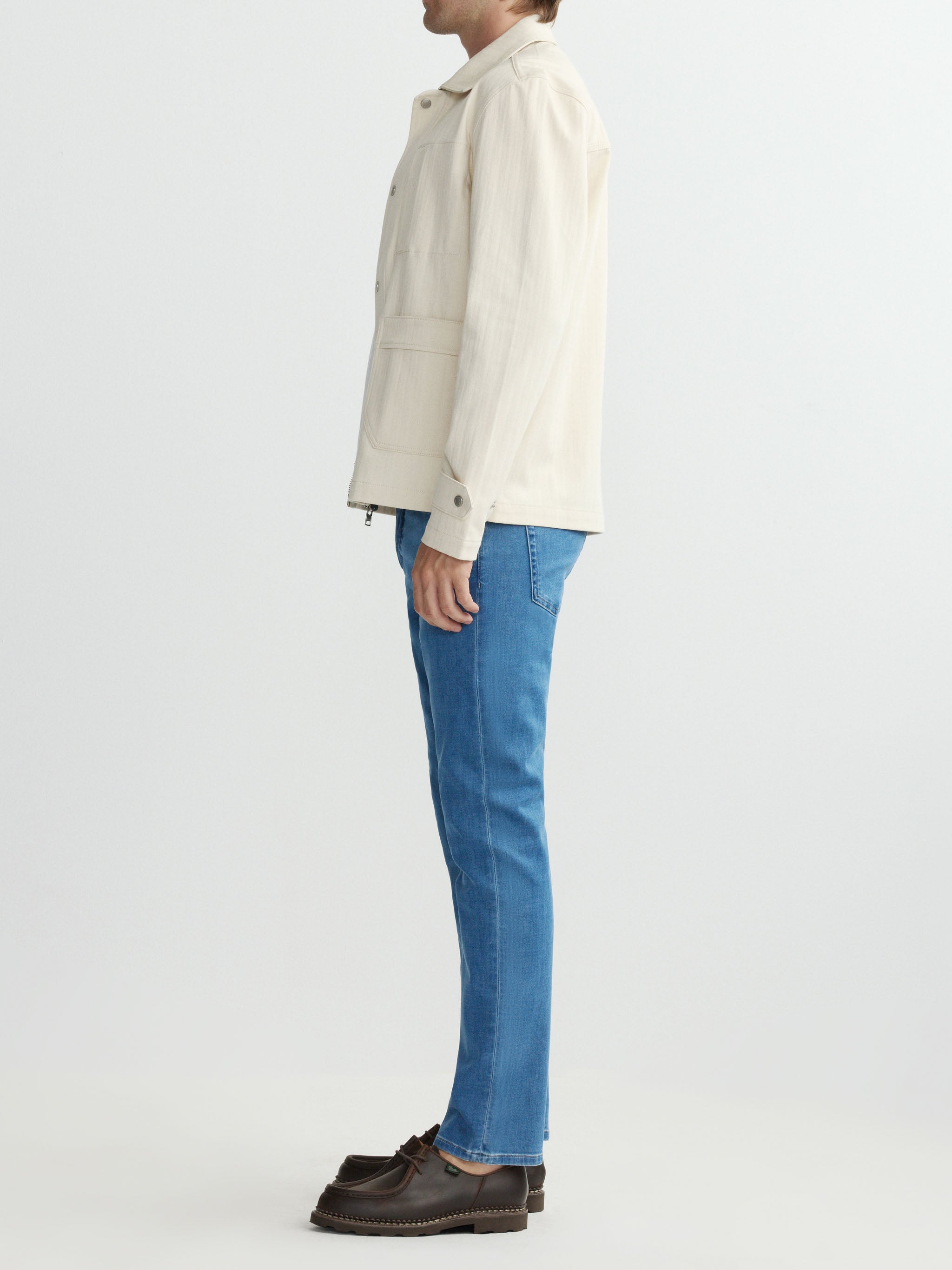 Person wearing a white jacket and blue jeans on a plain background