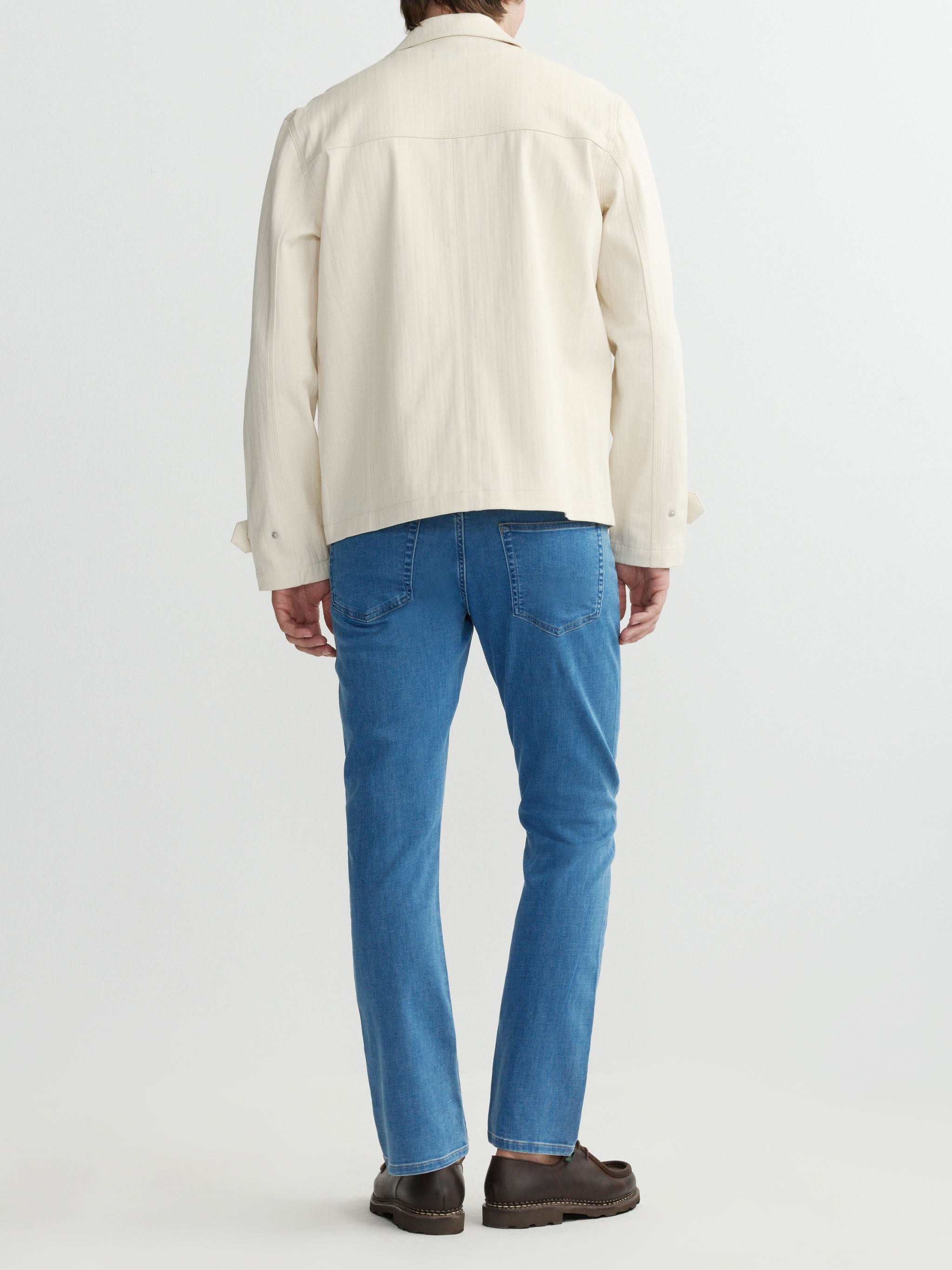 Person wearing a cream jacket and blue jeans on a white background