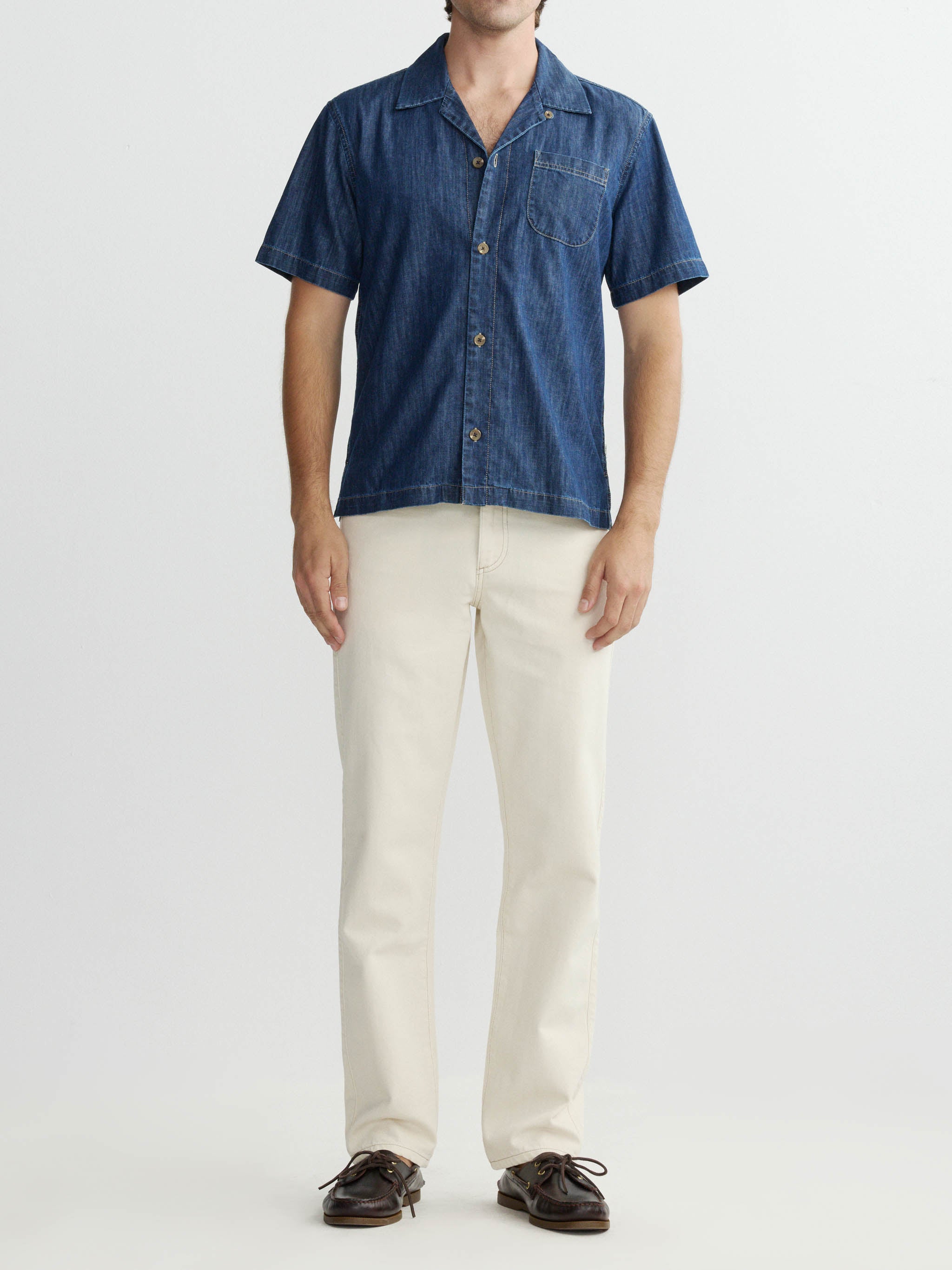 Person wearing a blue denim shirt and beige pants on a white background