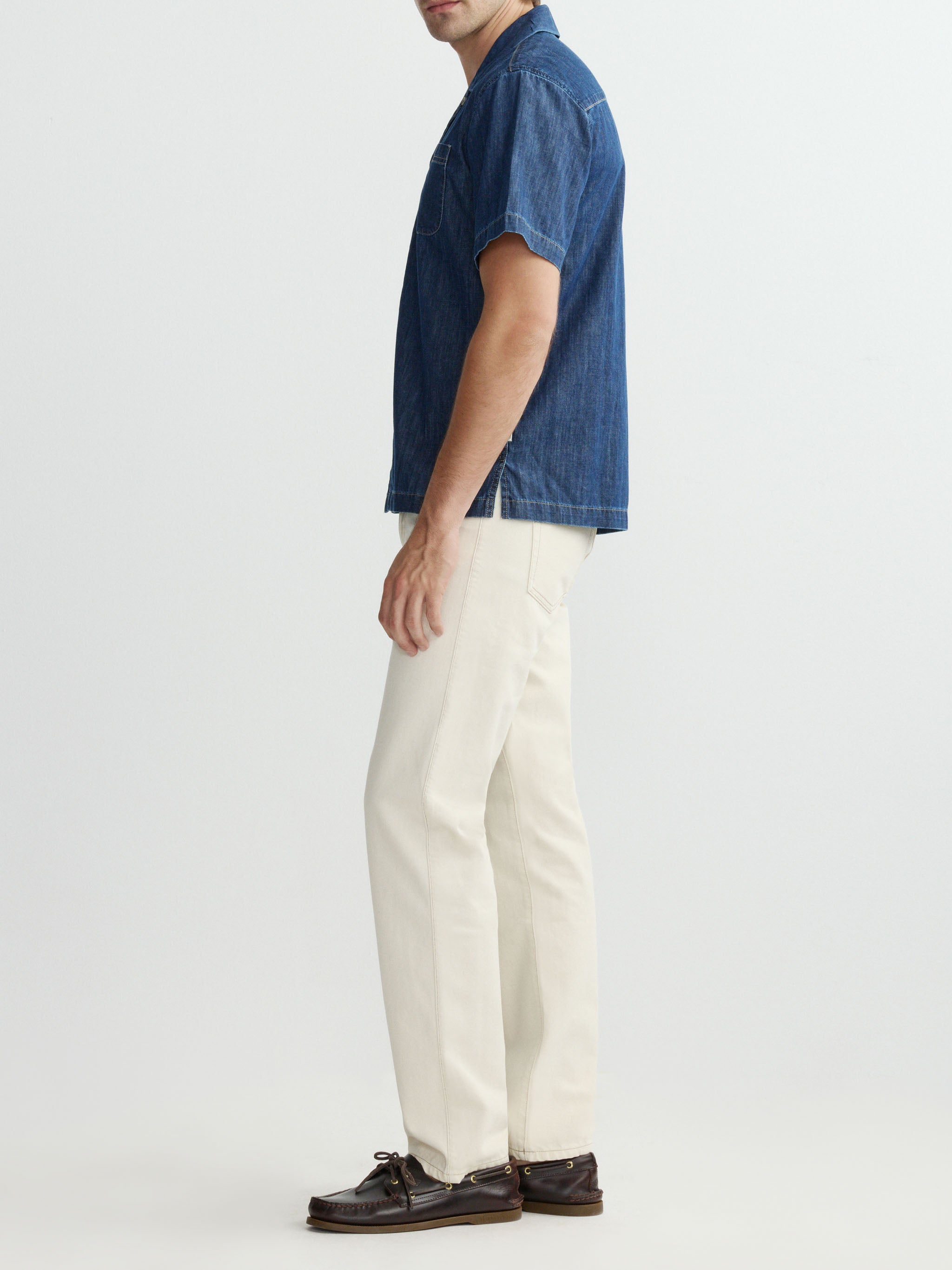 Man wearing a blue denim shirt and white pants on a light gray background
