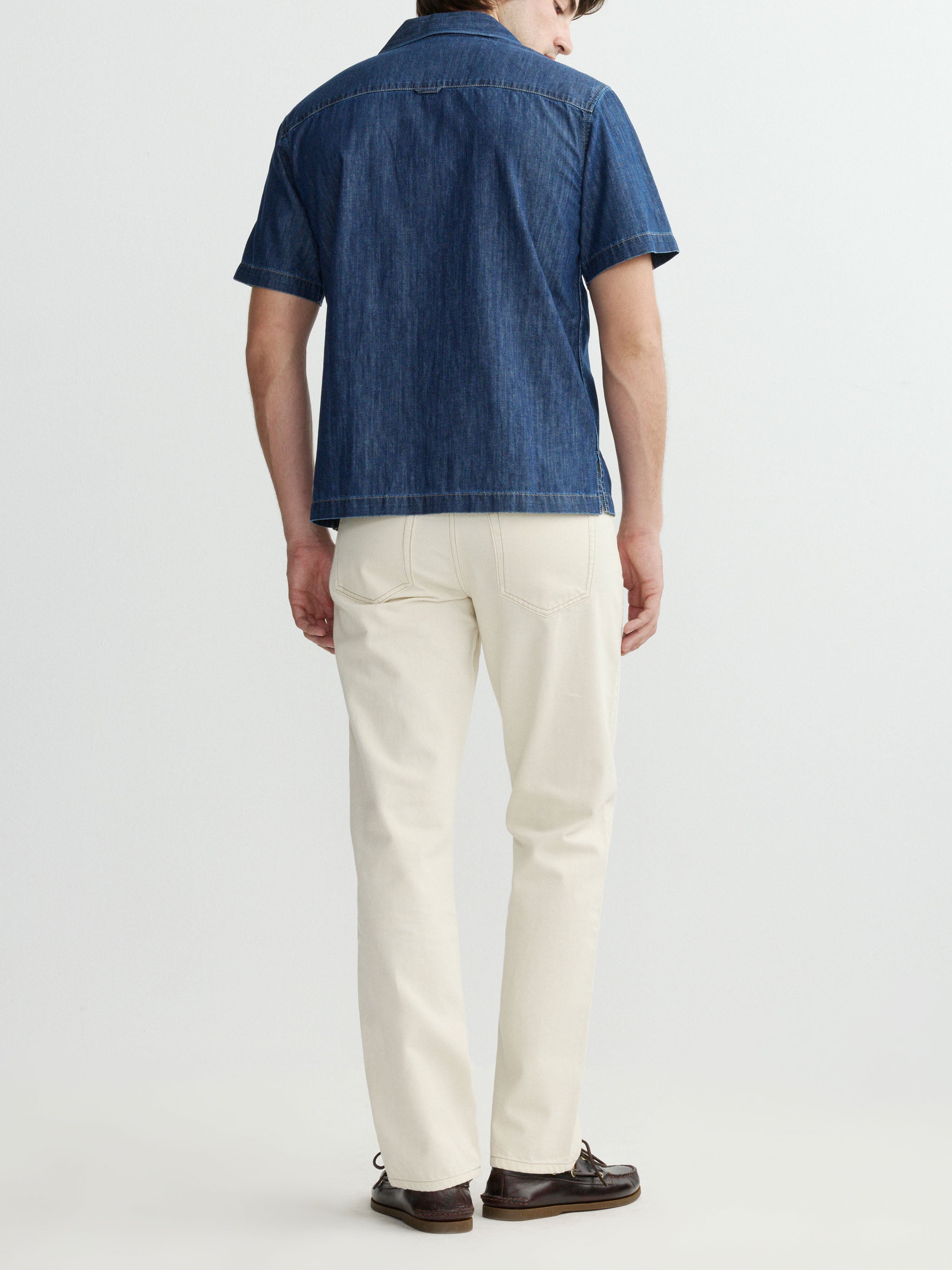 Person wearing a blue denim shirt and white pants on a light gray background