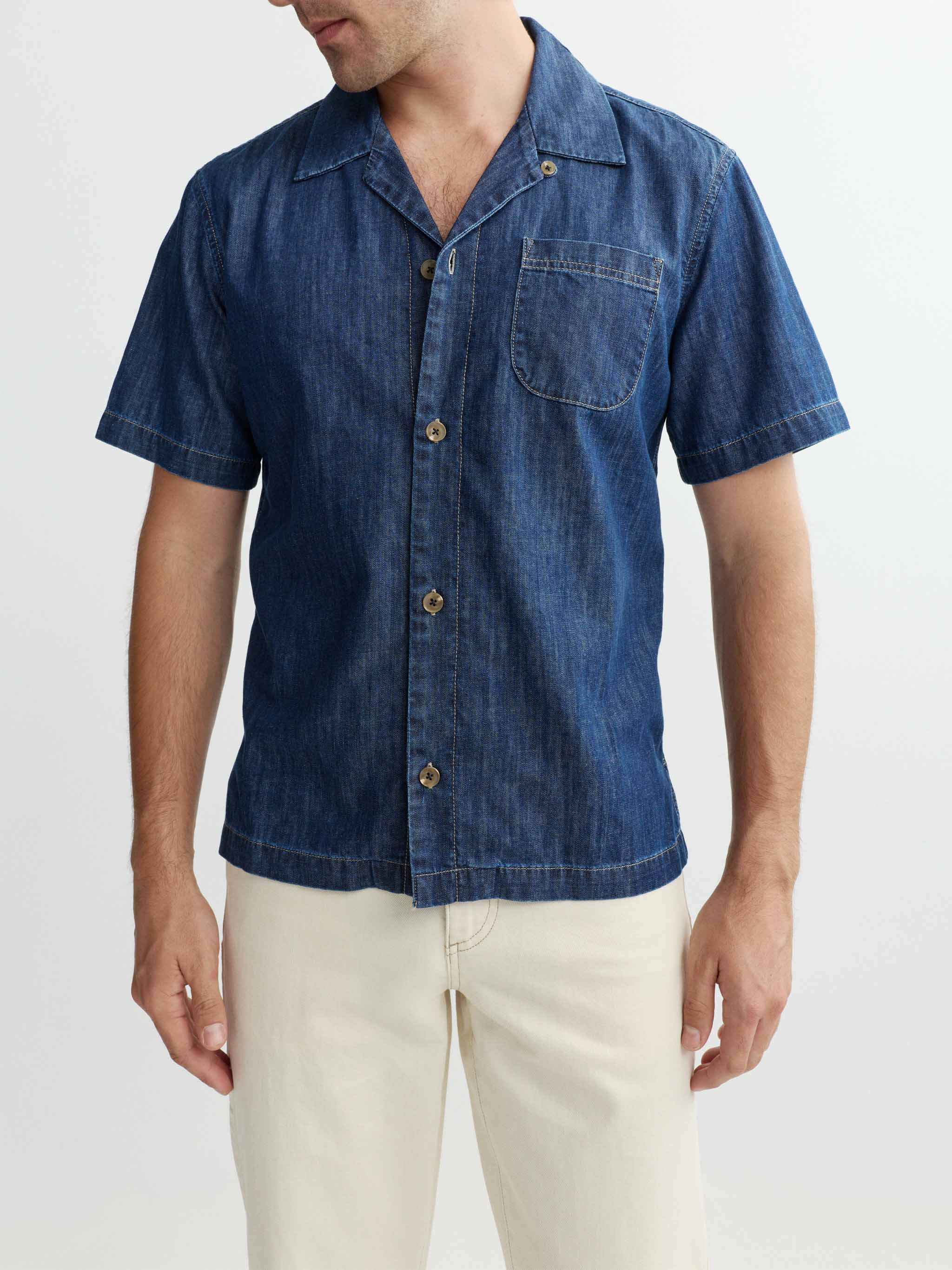 Man wearing a blue denim shirt with beige pants on a light gray background