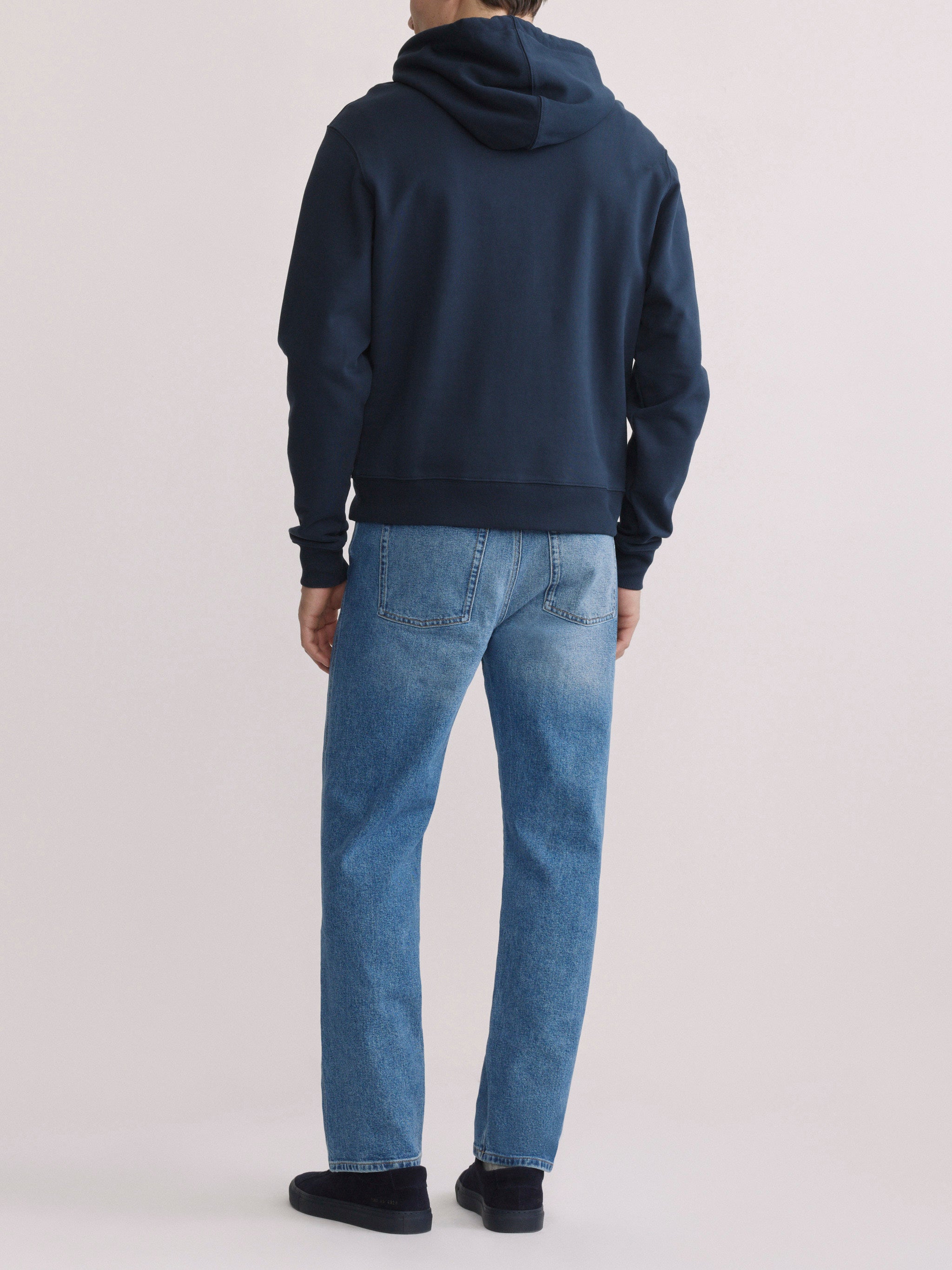 DL1961 men's Chris modern straight jeans in light blue 'Stonecut', full-length back view with navy hoodie.