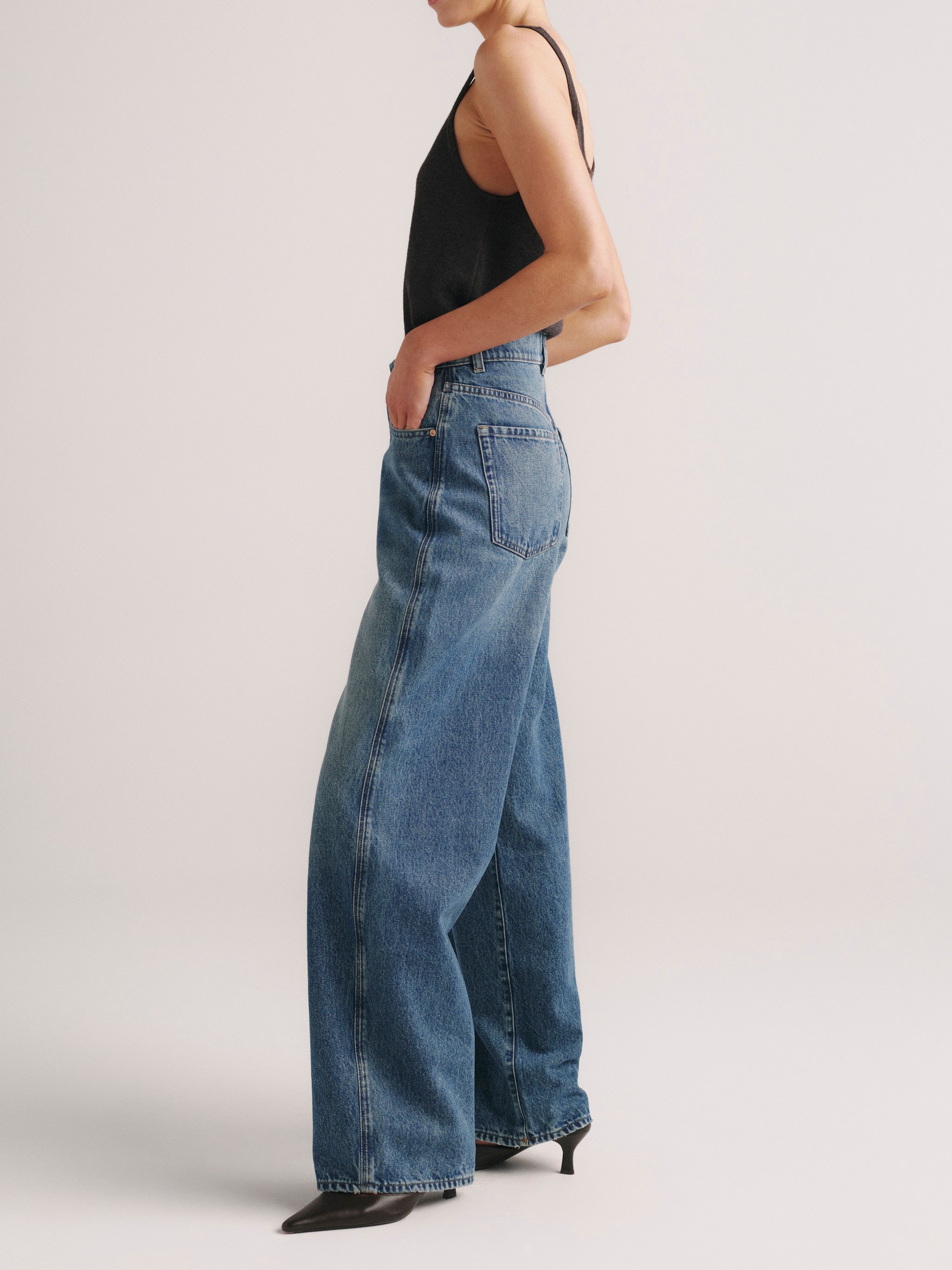 Person wearing blue jeans and a black top on a plain background