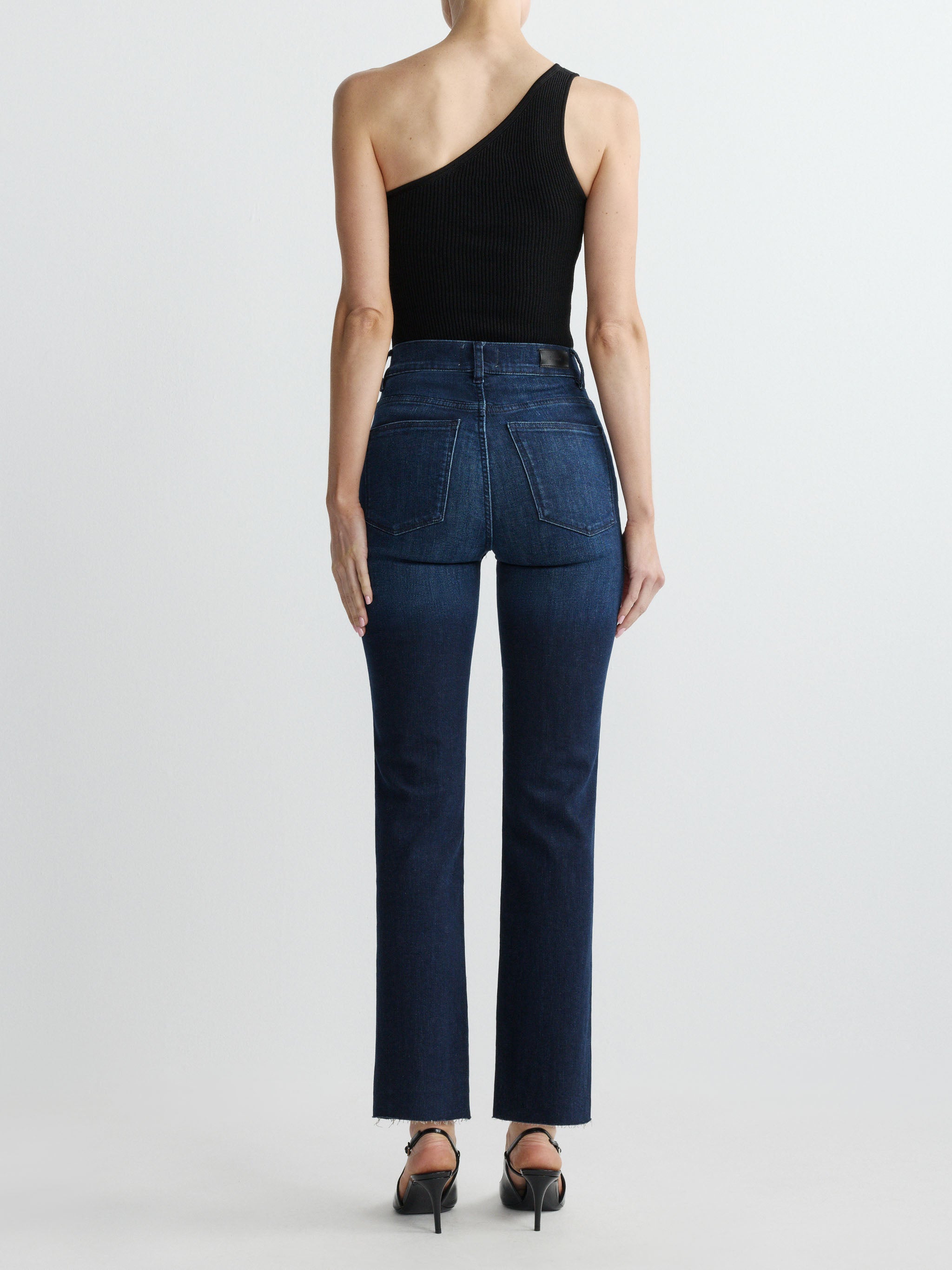 Person wearing dark blue jeans and a black one-shoulder top on a white background