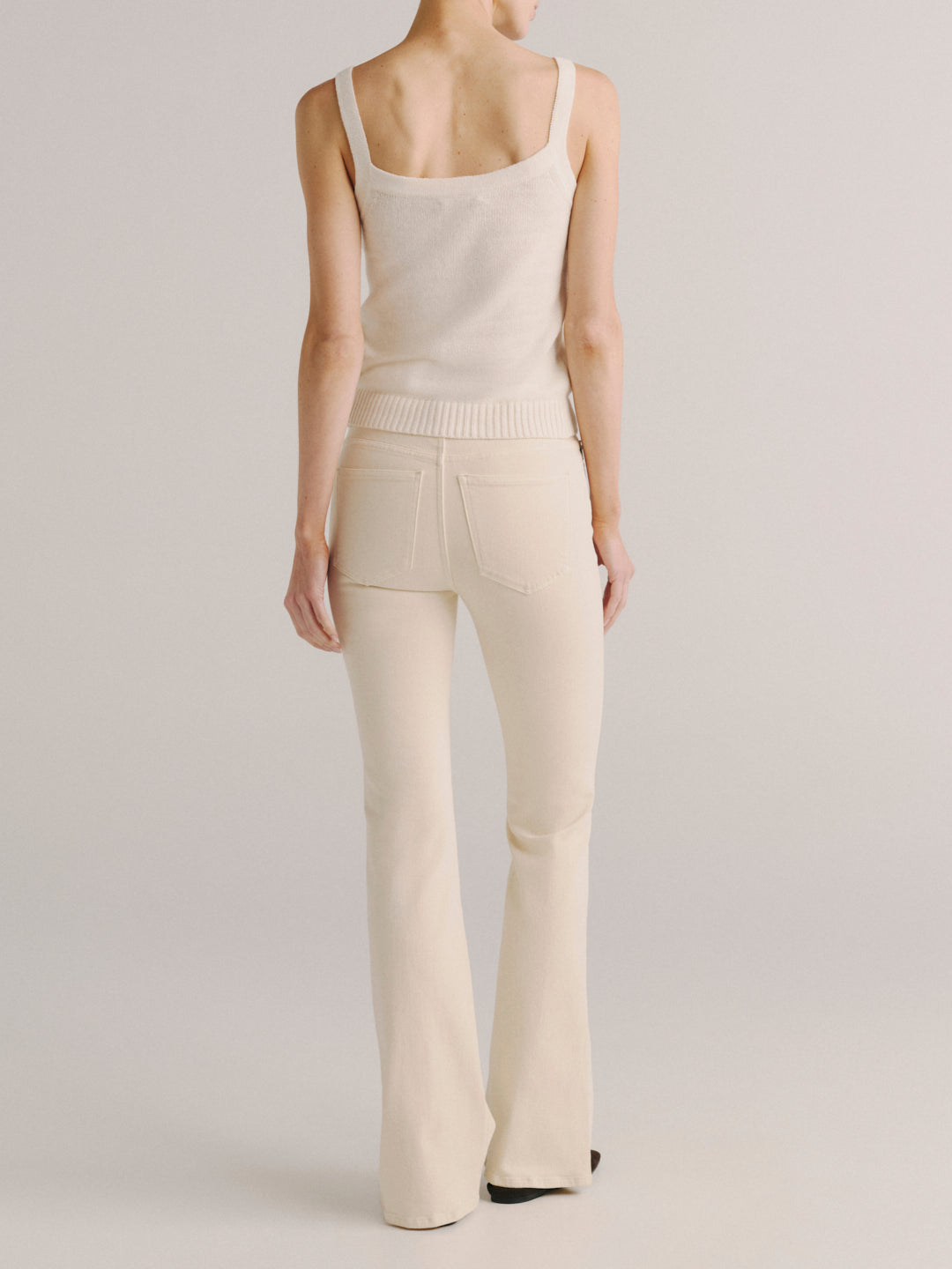 A model shown from the back wearing a cream-colored knit tank top and matching cream flared pants against a light gray studio background.