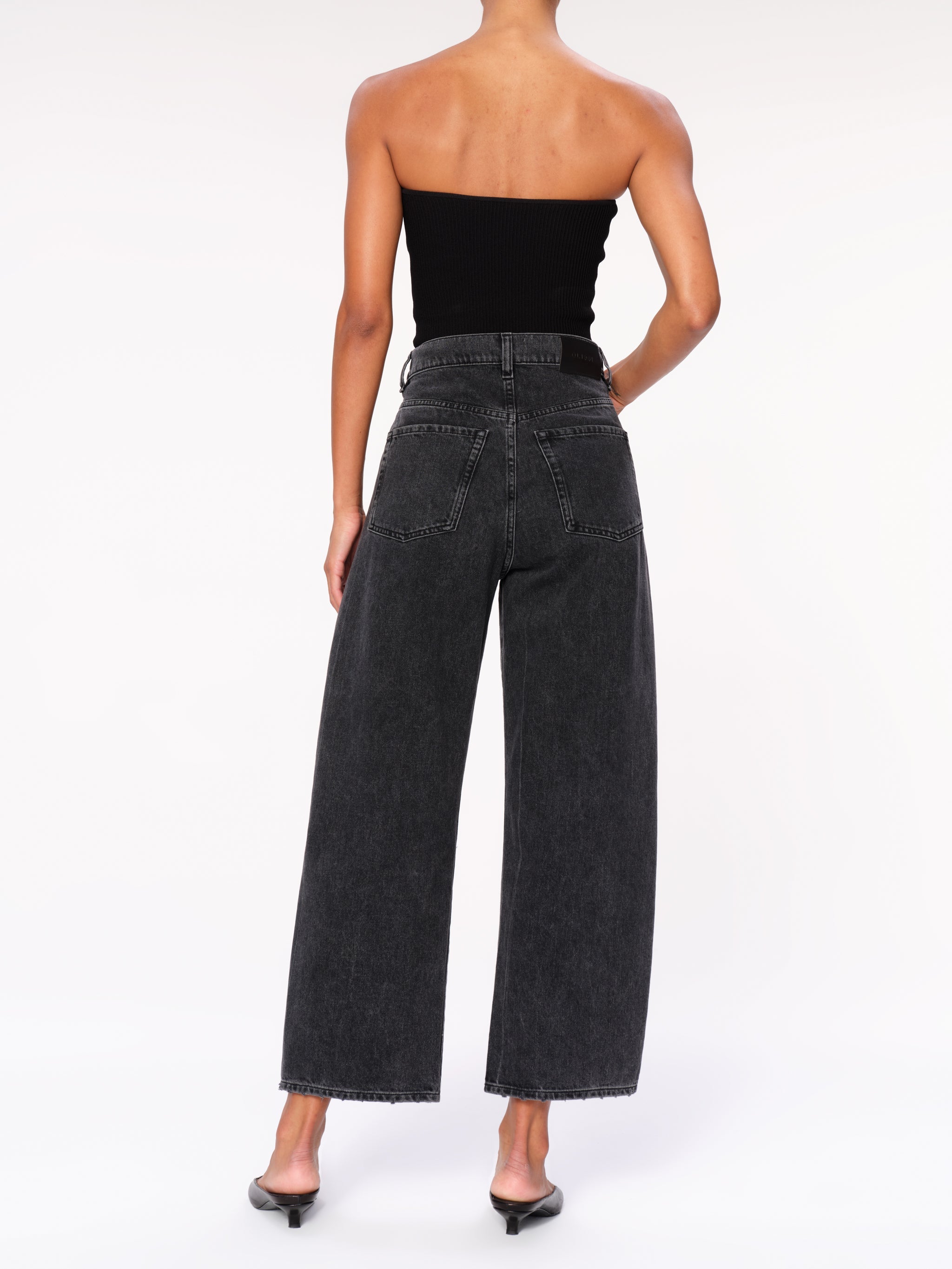Taylor jeans in Nightshade on a model in a black tube top, full-length back three-quarter view.