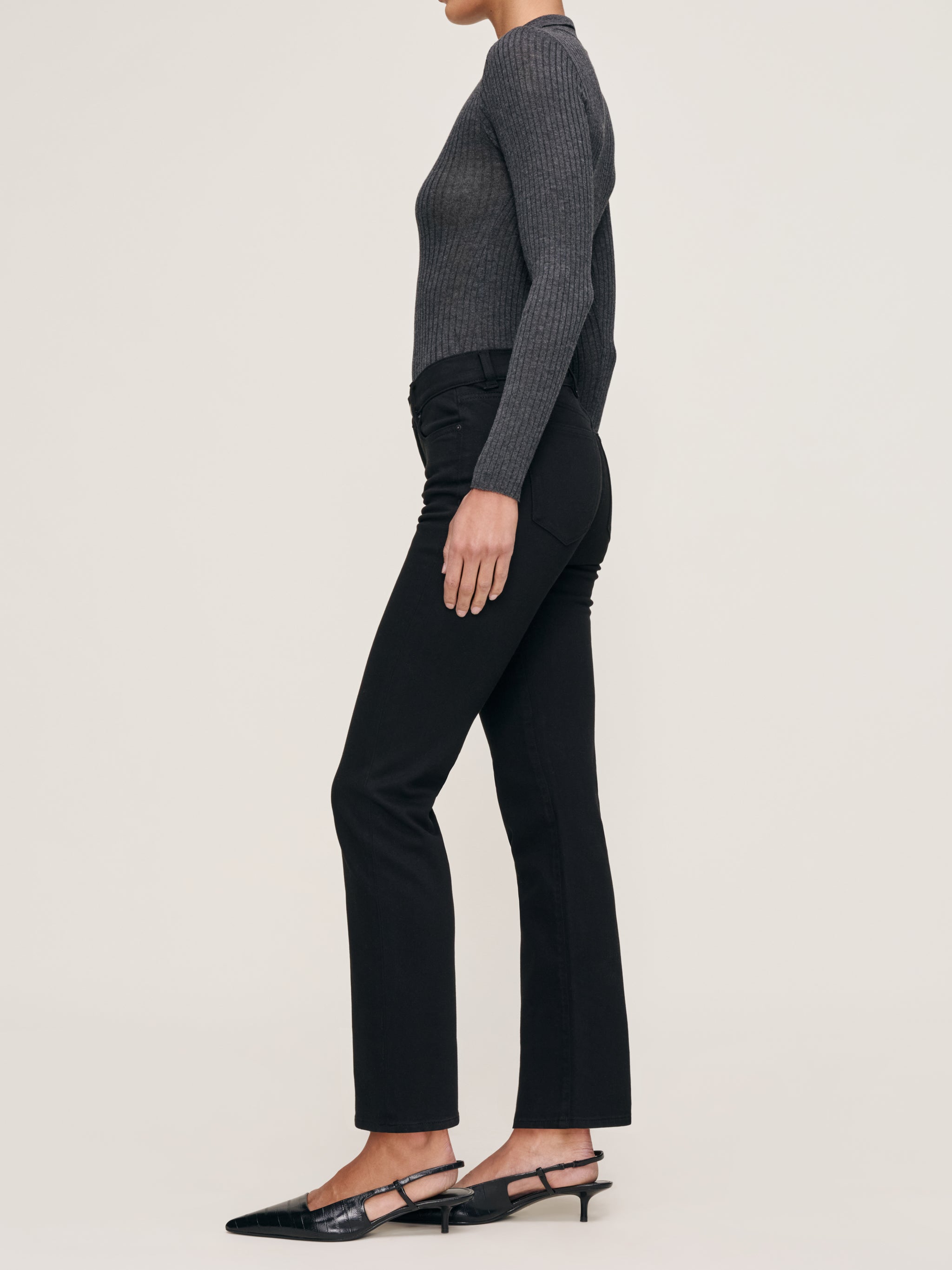 Mara jeans in Black on a model in a grey knit polo, full-length side profile in a studio.