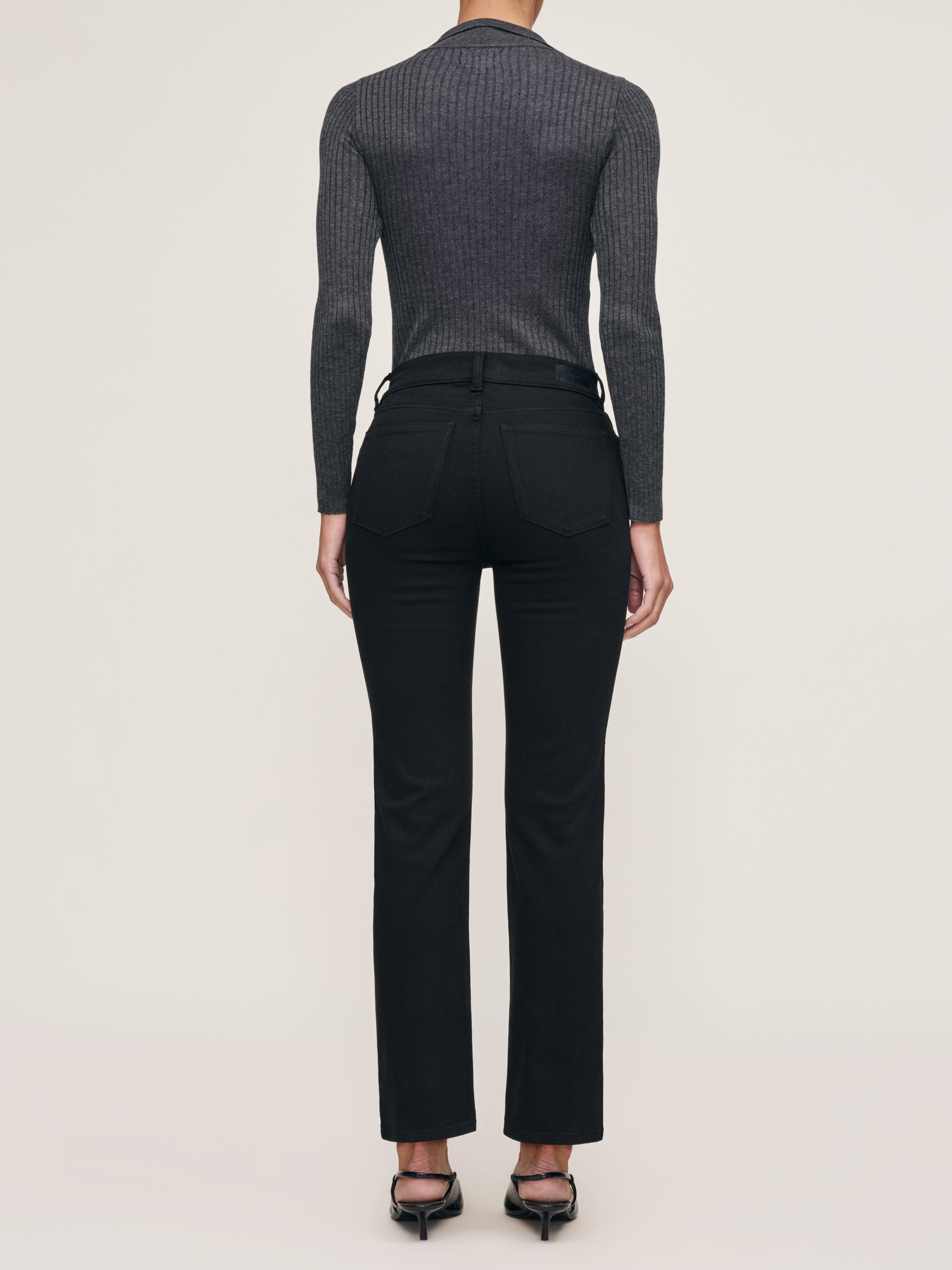 Mara jeans in Black on a model in a grey knit polo, full-length back view in a studio.