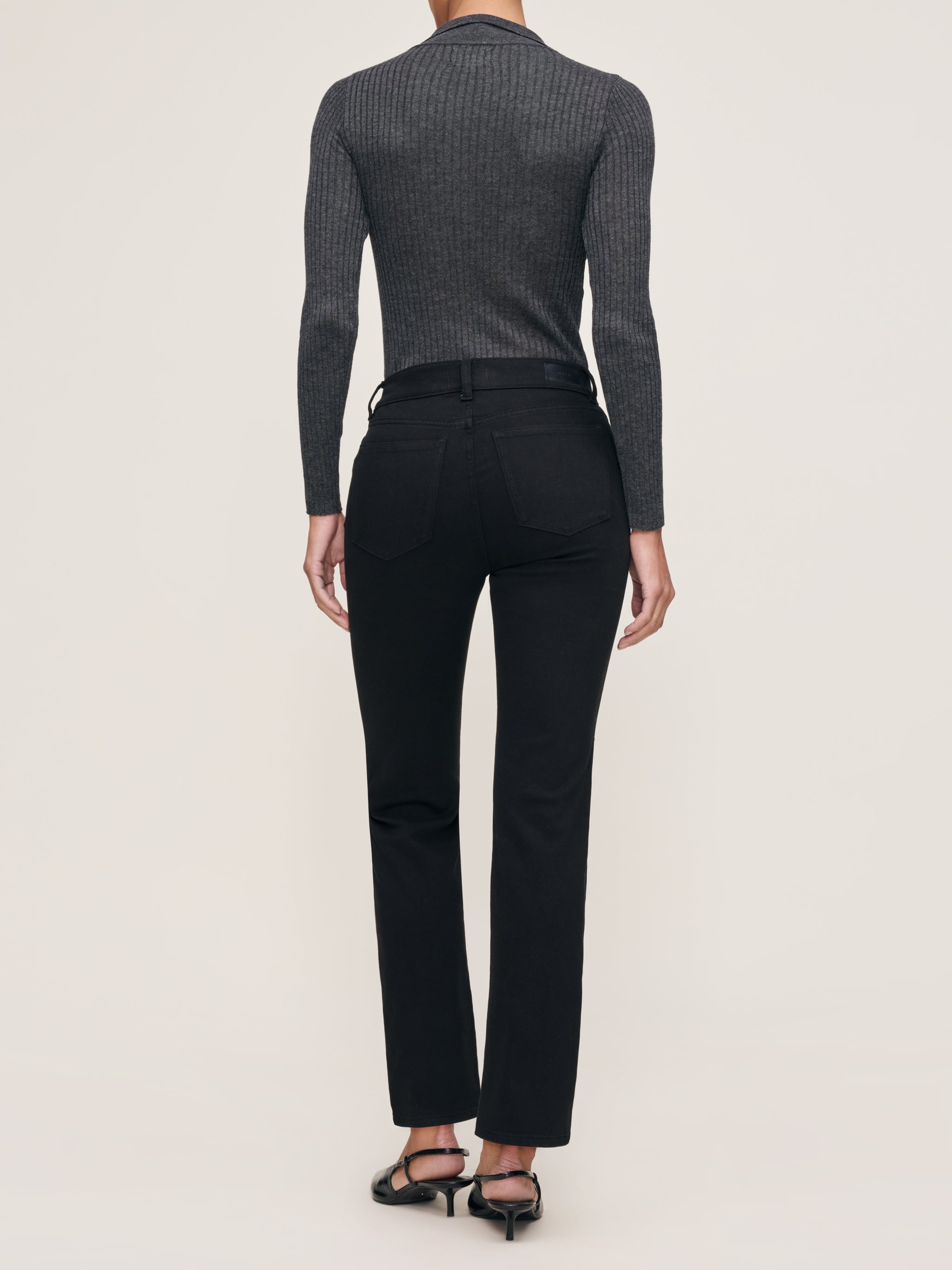 Mara jeans in Black on a model in a grey knit polo, full-length back view in a studio.