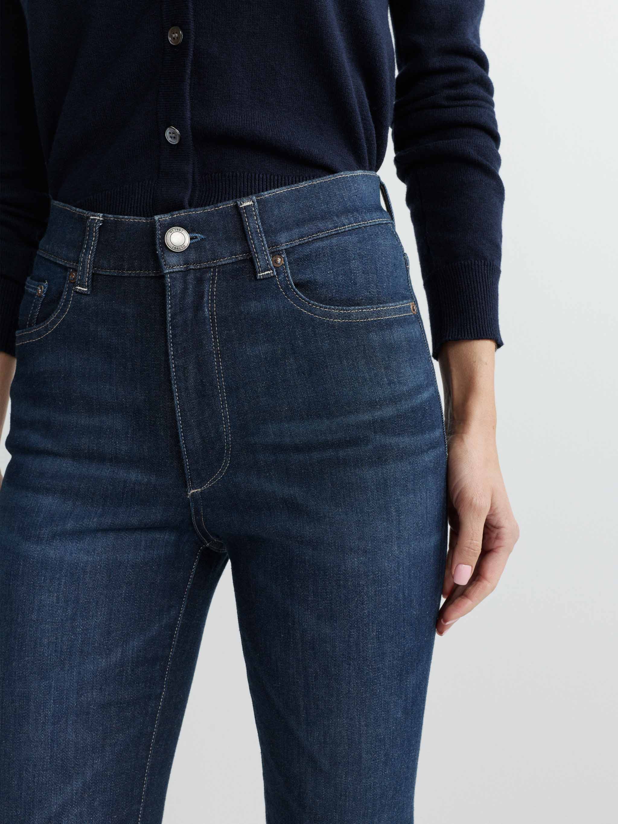 Person wearing dark blue jeans with a plain background