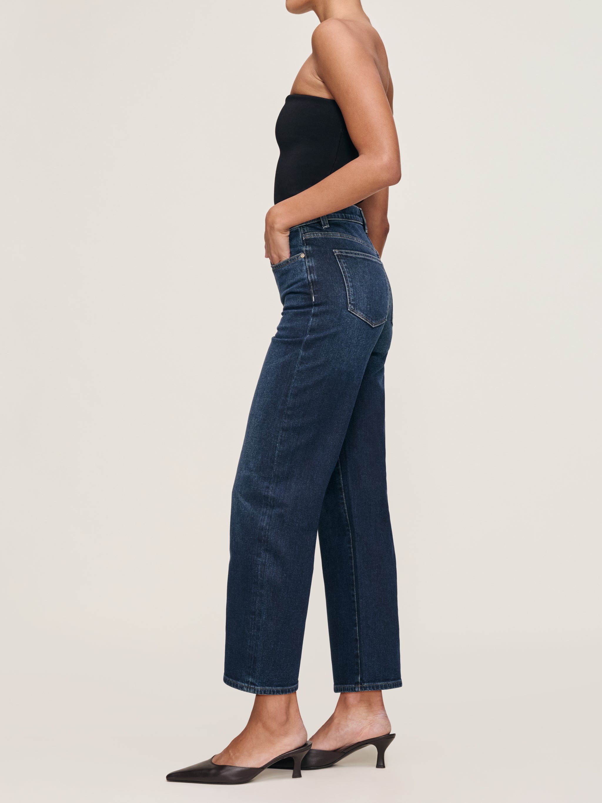 Karmine jeans in Dark Sea on a model with a black tube top, full-length side view in a studio.