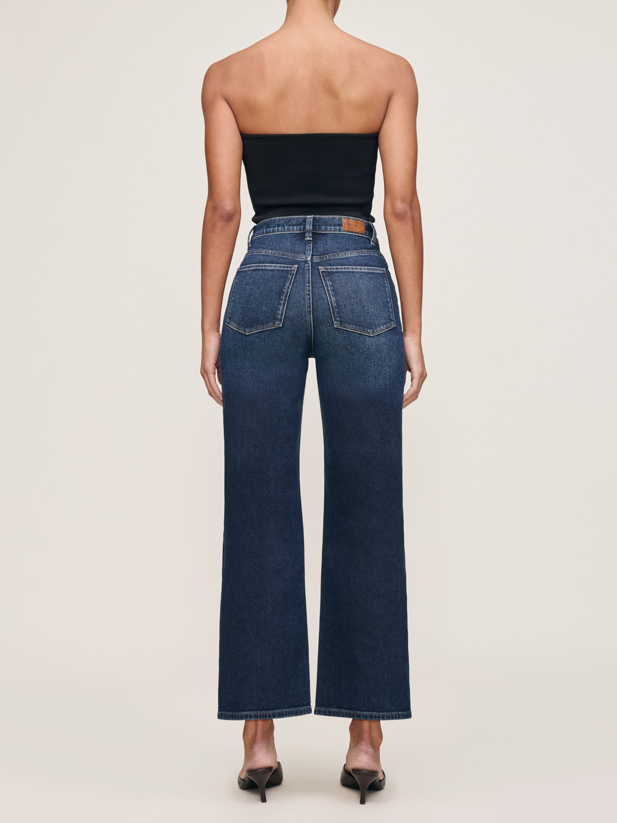 Karmine jeans in Dark Sea on a model with a black tube top, full-length back view in a studio.