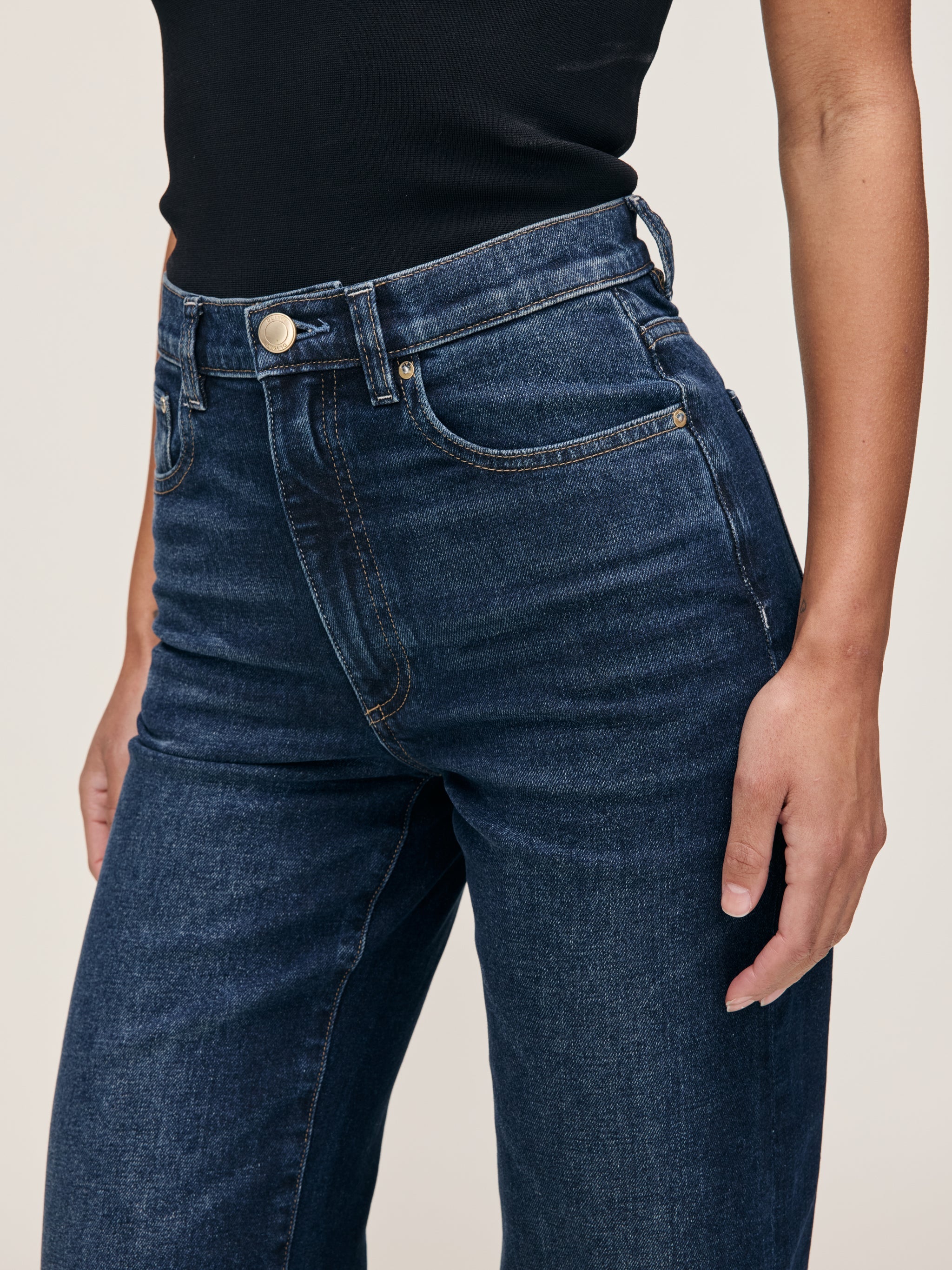 Karmine jeans in Dark Sea on a model, close-up front view of the waist and pocket in a studio.