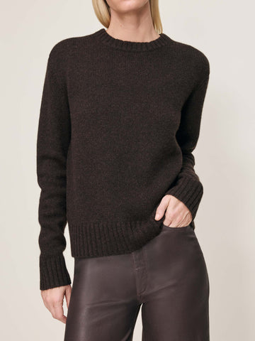Person wearing a dark brown sweater and brown pants against a plain background