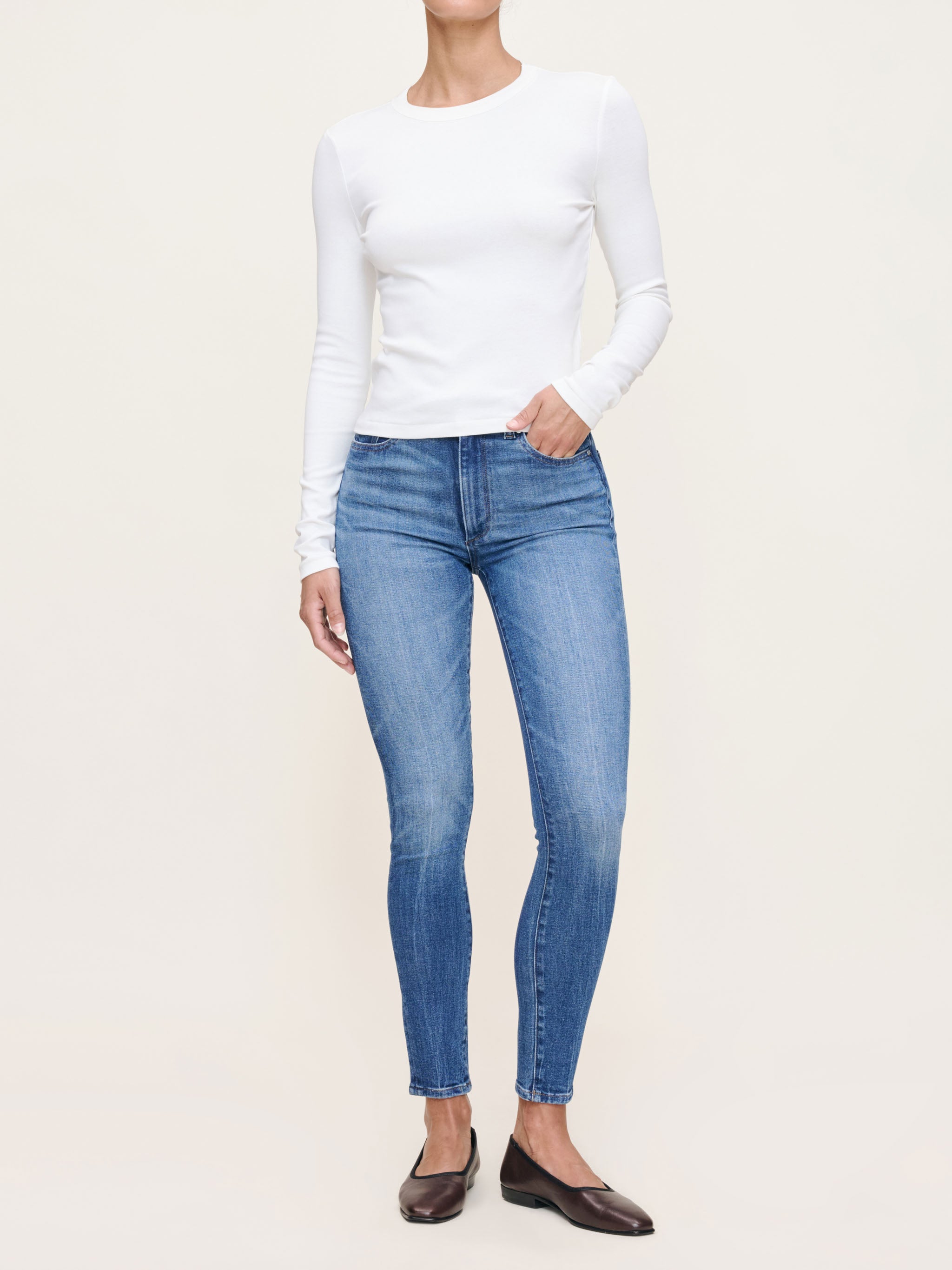 Person wearing a white long-sleeve top and blue jeans on a plain background