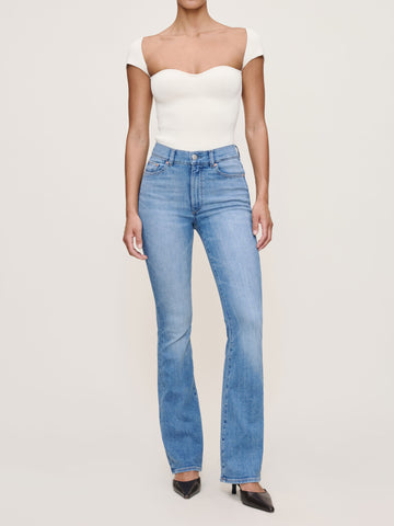 Person wearing a white off-shoulder top and blue jeans on a plain background