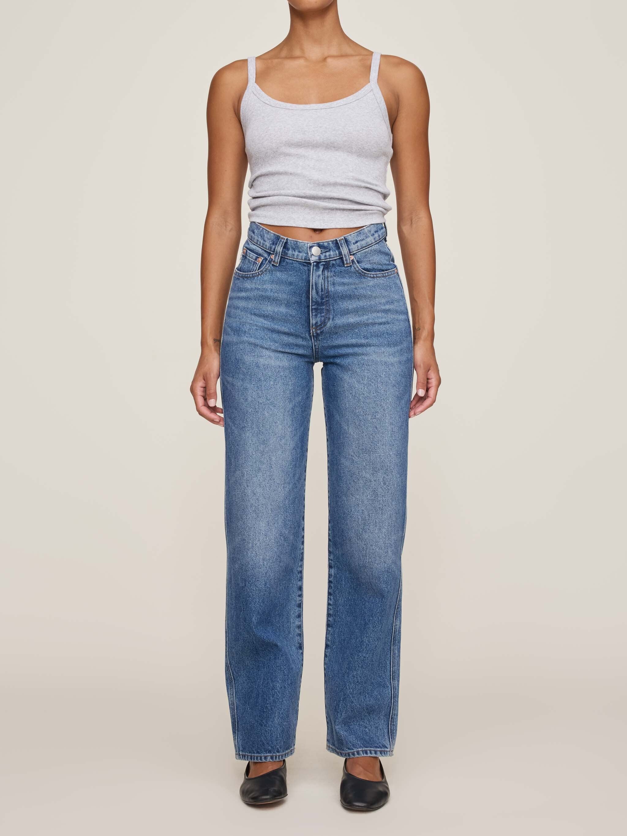 Person wearing a light gray tank top and blue jeans on a beige background