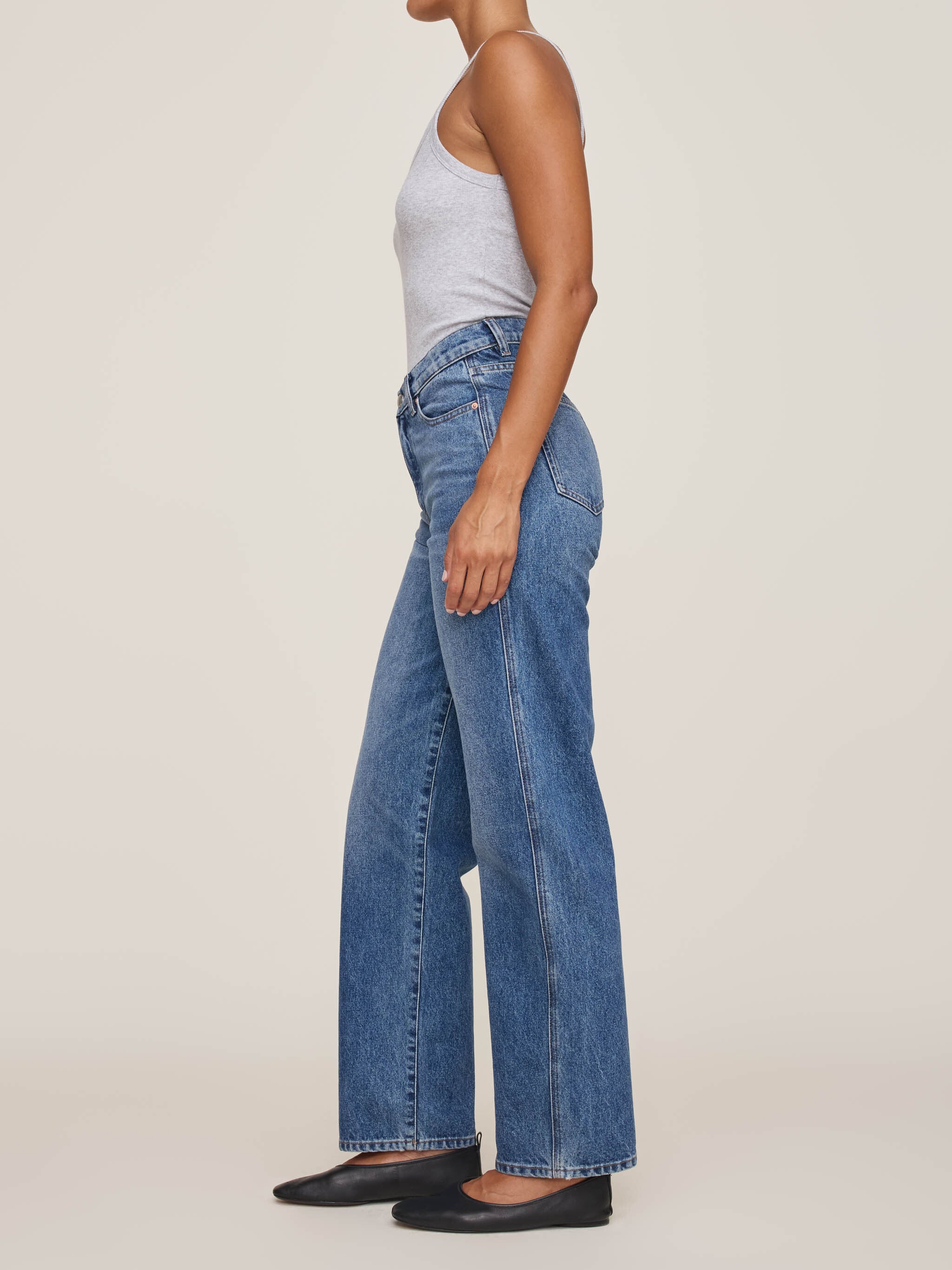 Person wearing blue jeans and a gray top on a plain background