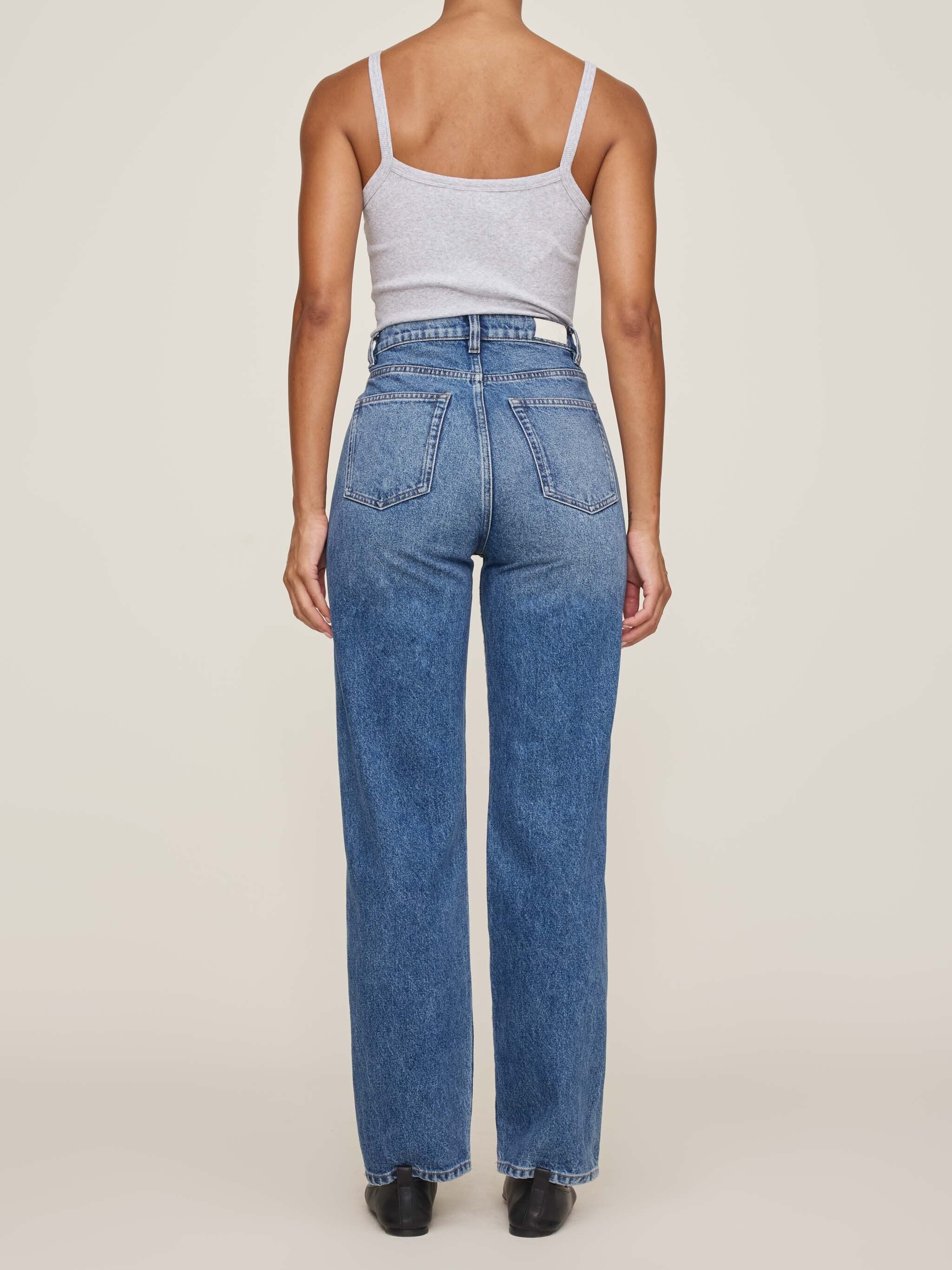 Person wearing blue jeans and a light gray tank top on a white background