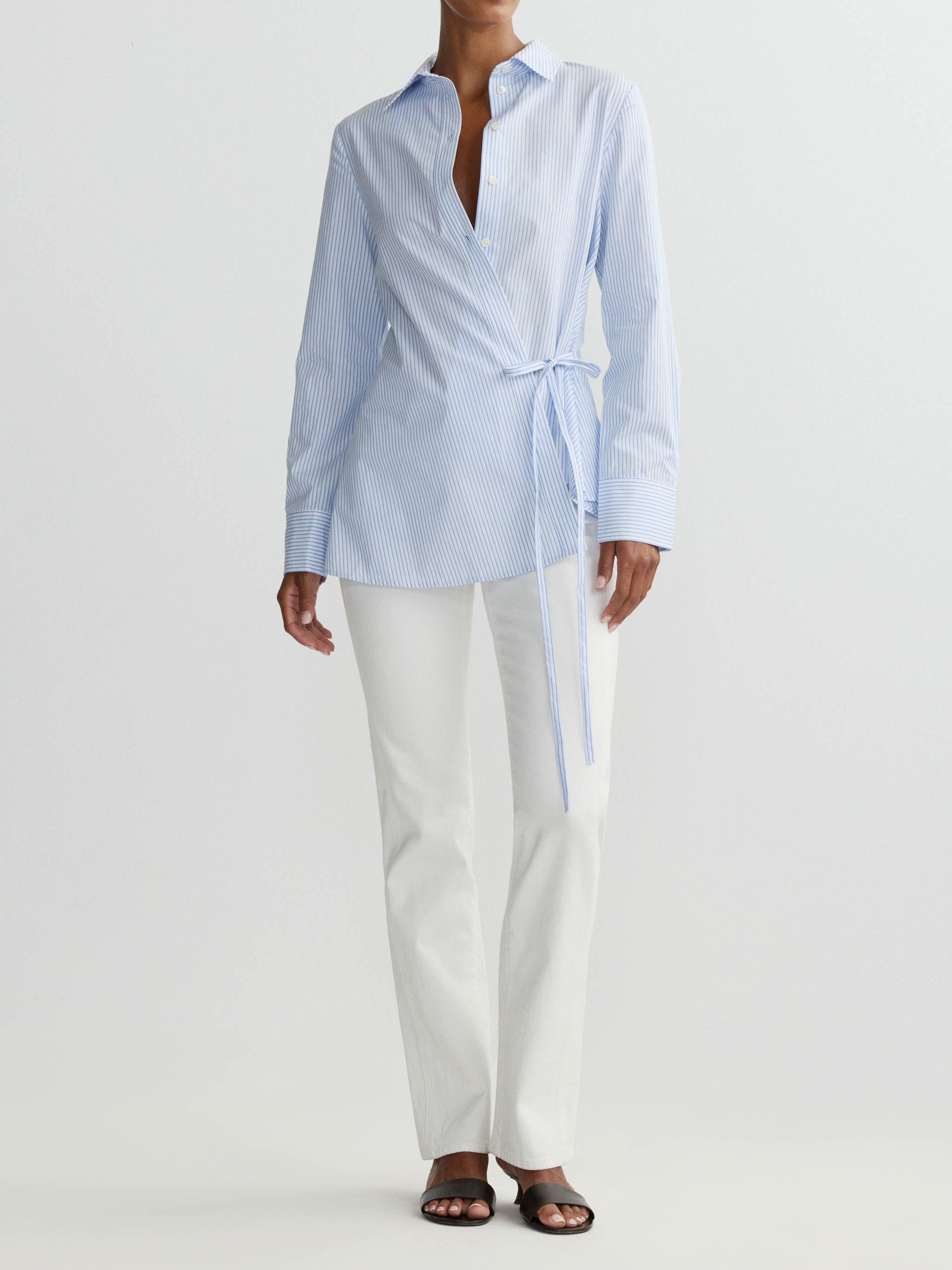 Person wearing a light blue button-up shirt with a tie and white pants on a white background