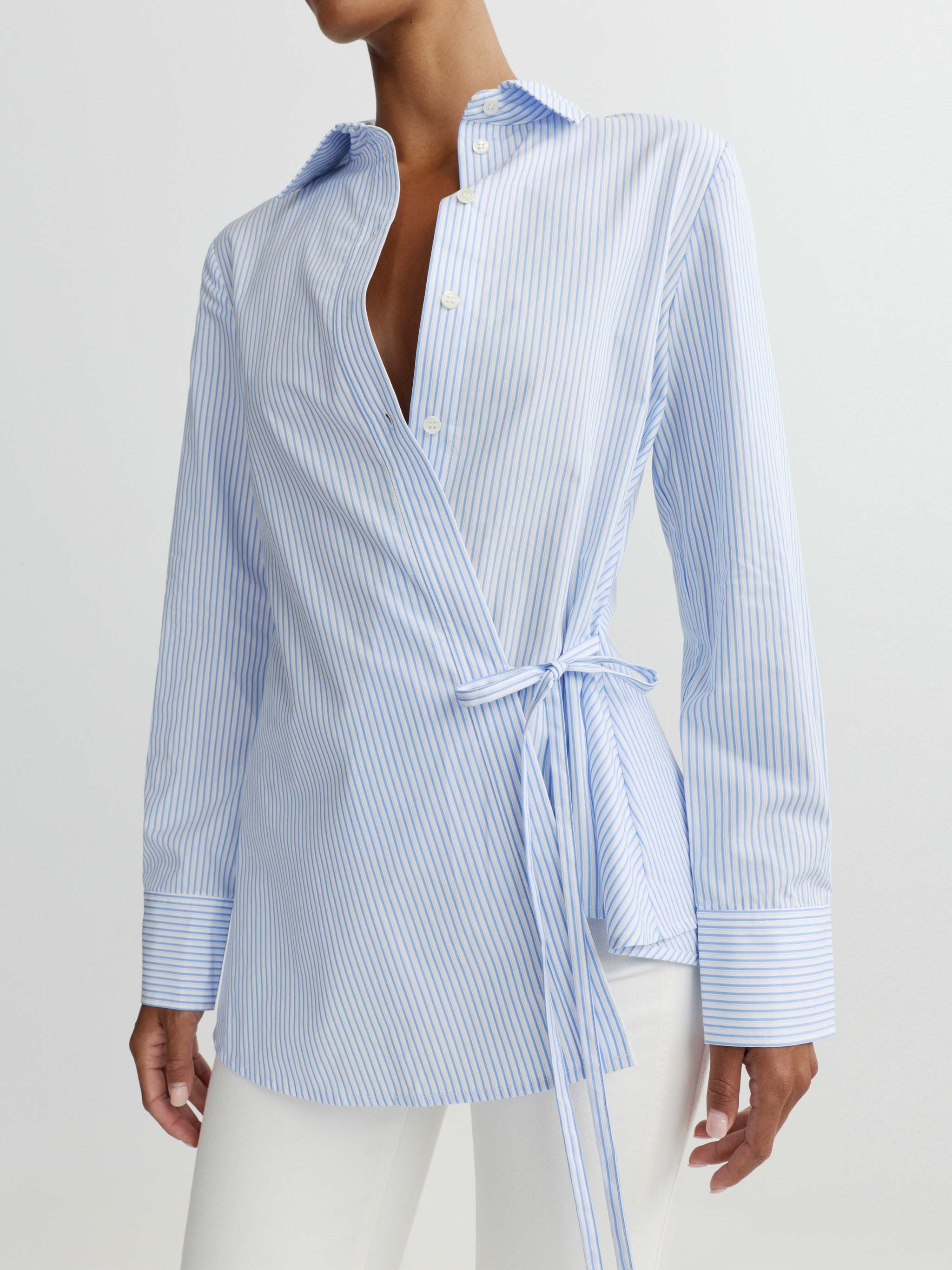 Woman wearing a blue and white striped shirt with a tie waist on a light gray background