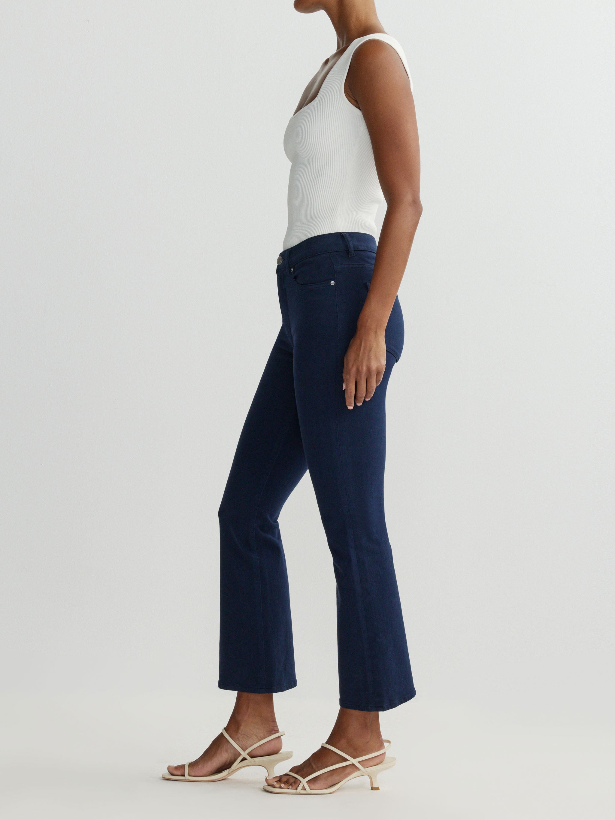 Person wearing navy blue jeans and a white top on a light gray background