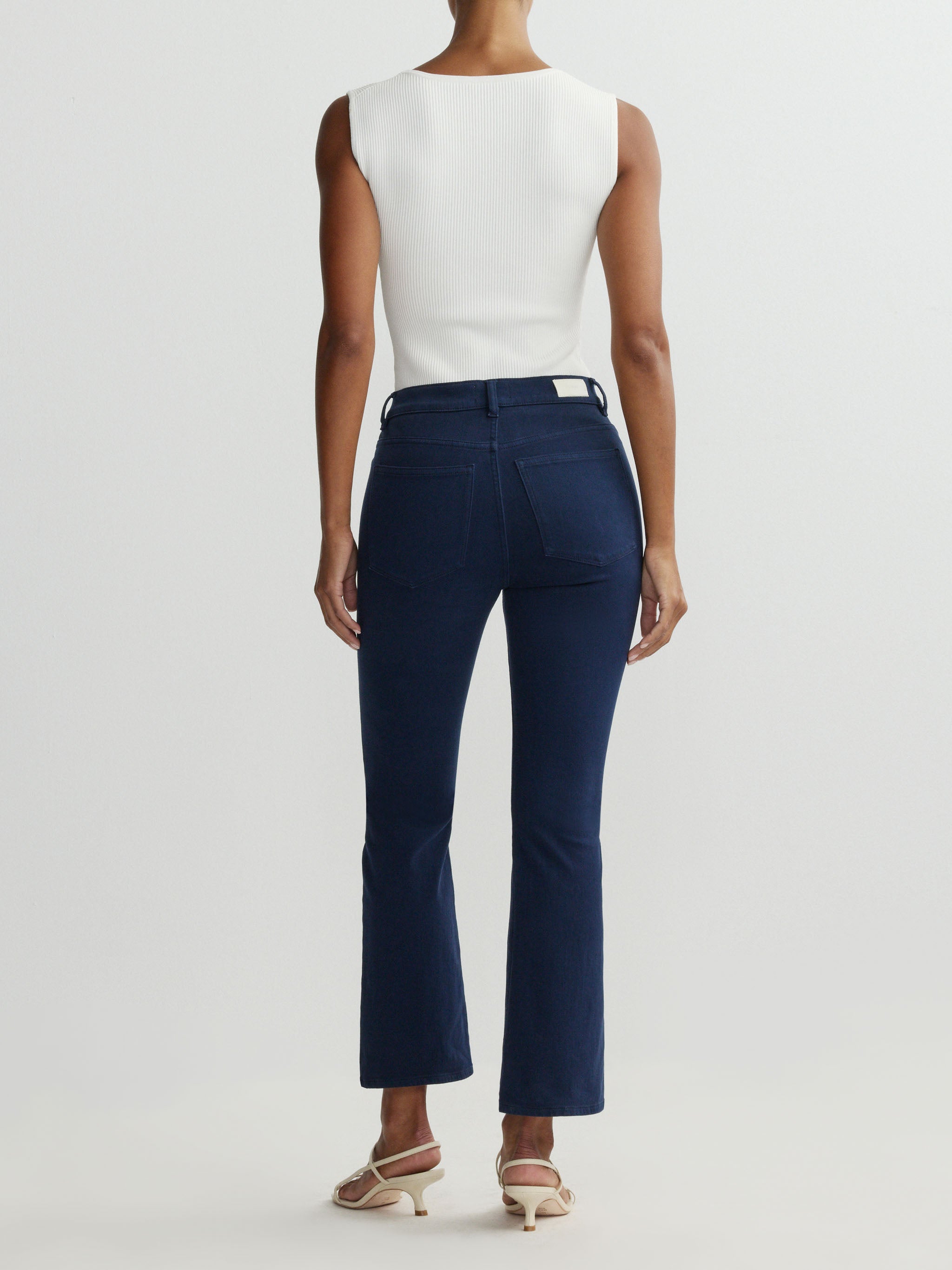 Person wearing navy pants and a white top on a light gray background