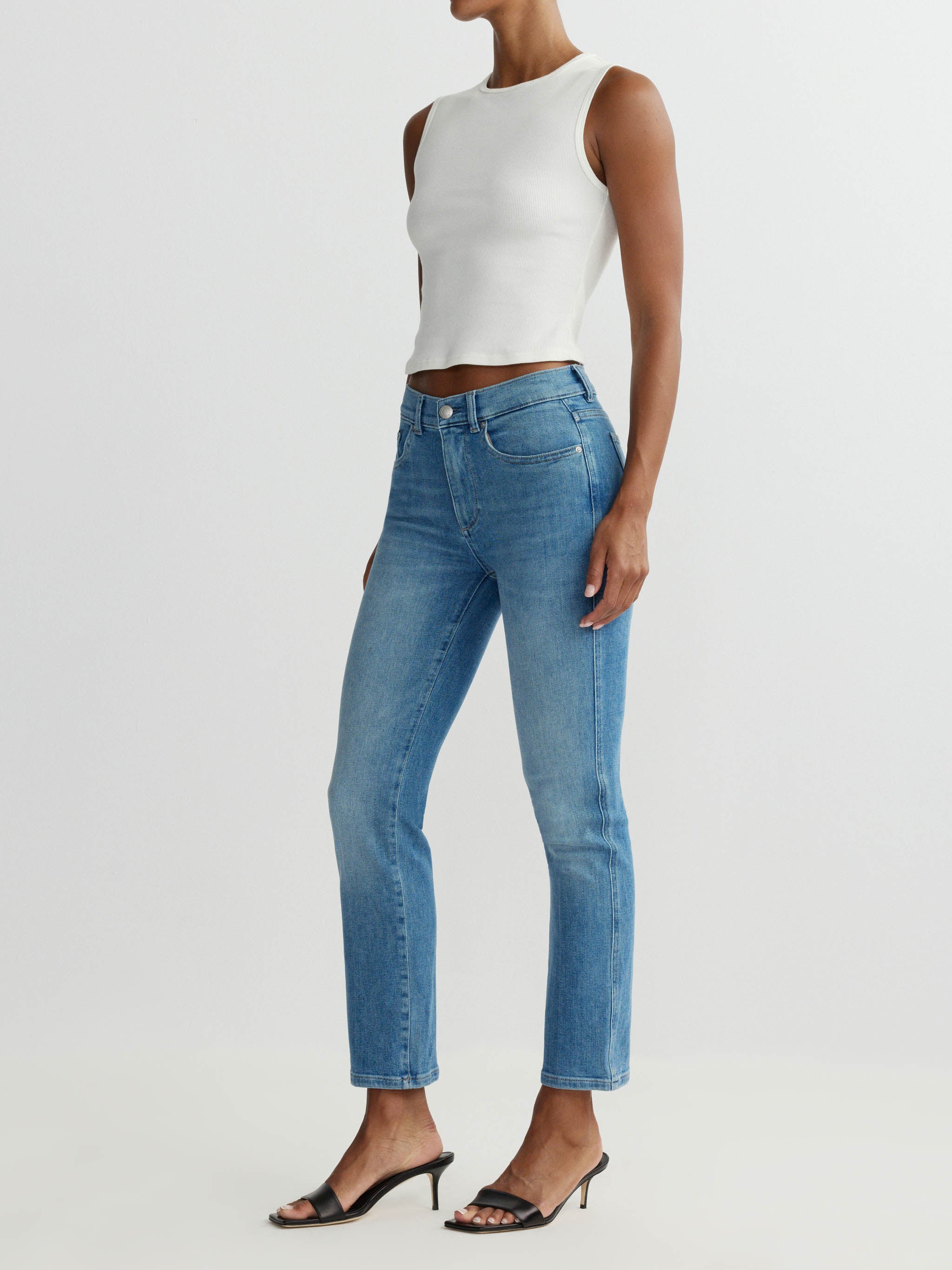 Person wearing a white sleeveless top and blue jeans on a light gray background