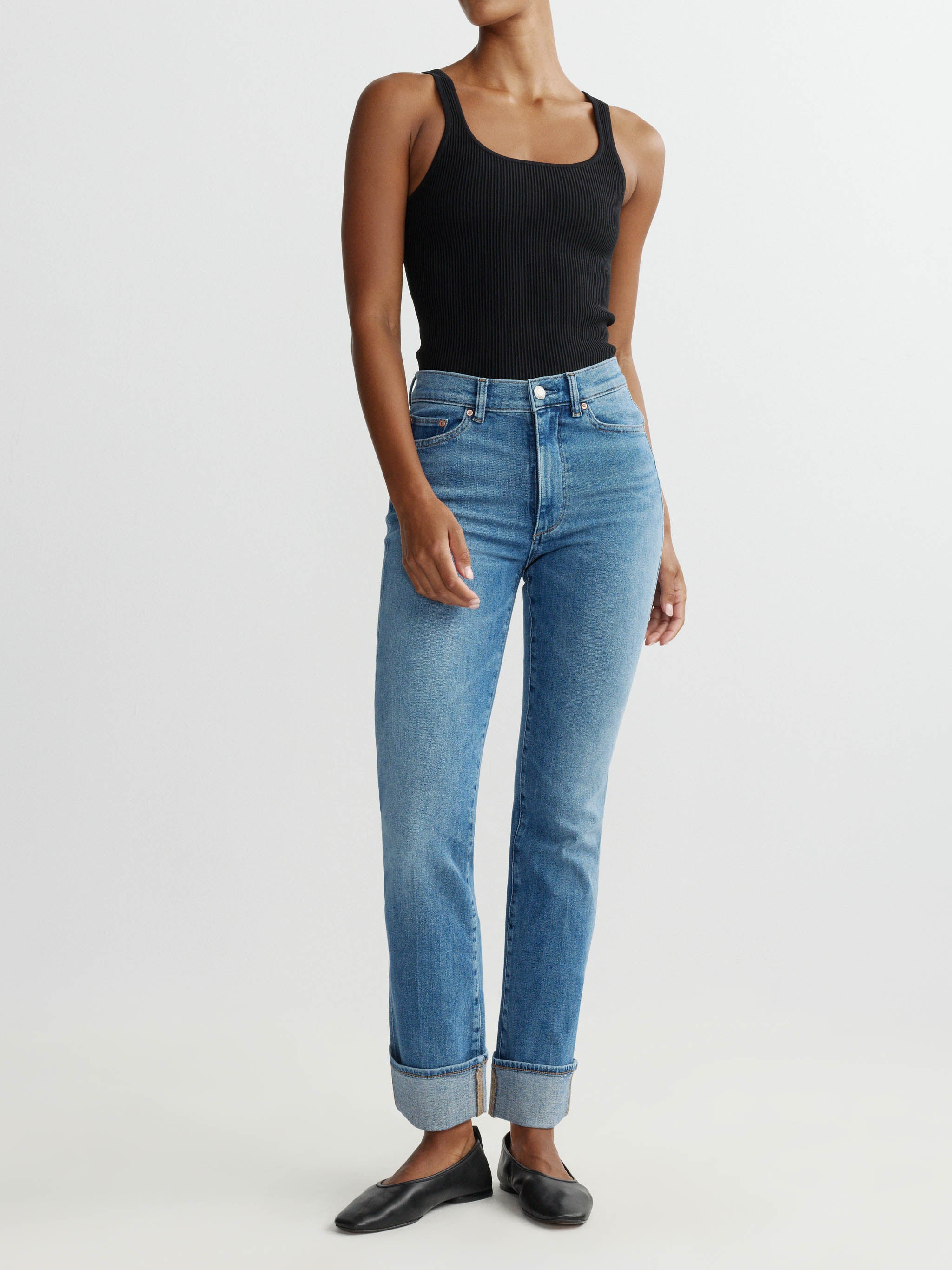Person wearing blue jeans and a black tank top on a white background