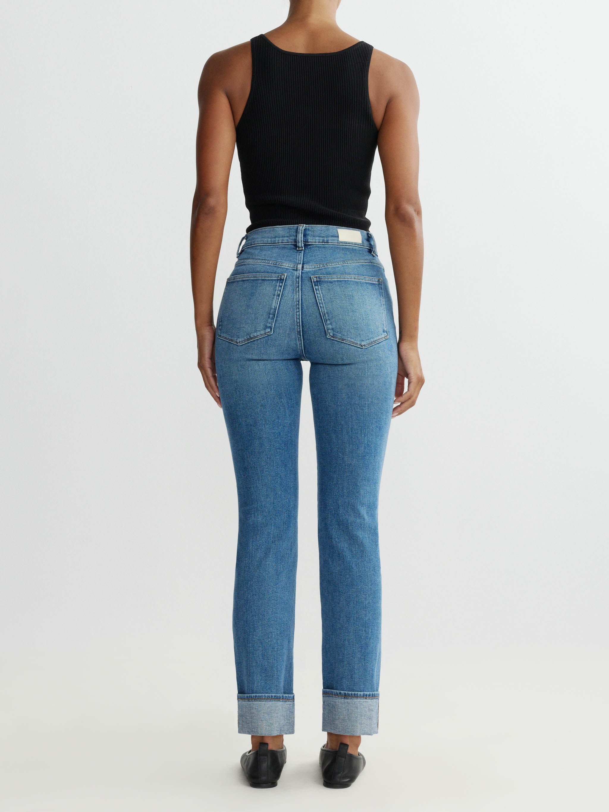 Person wearing blue jeans and a black top on a white background