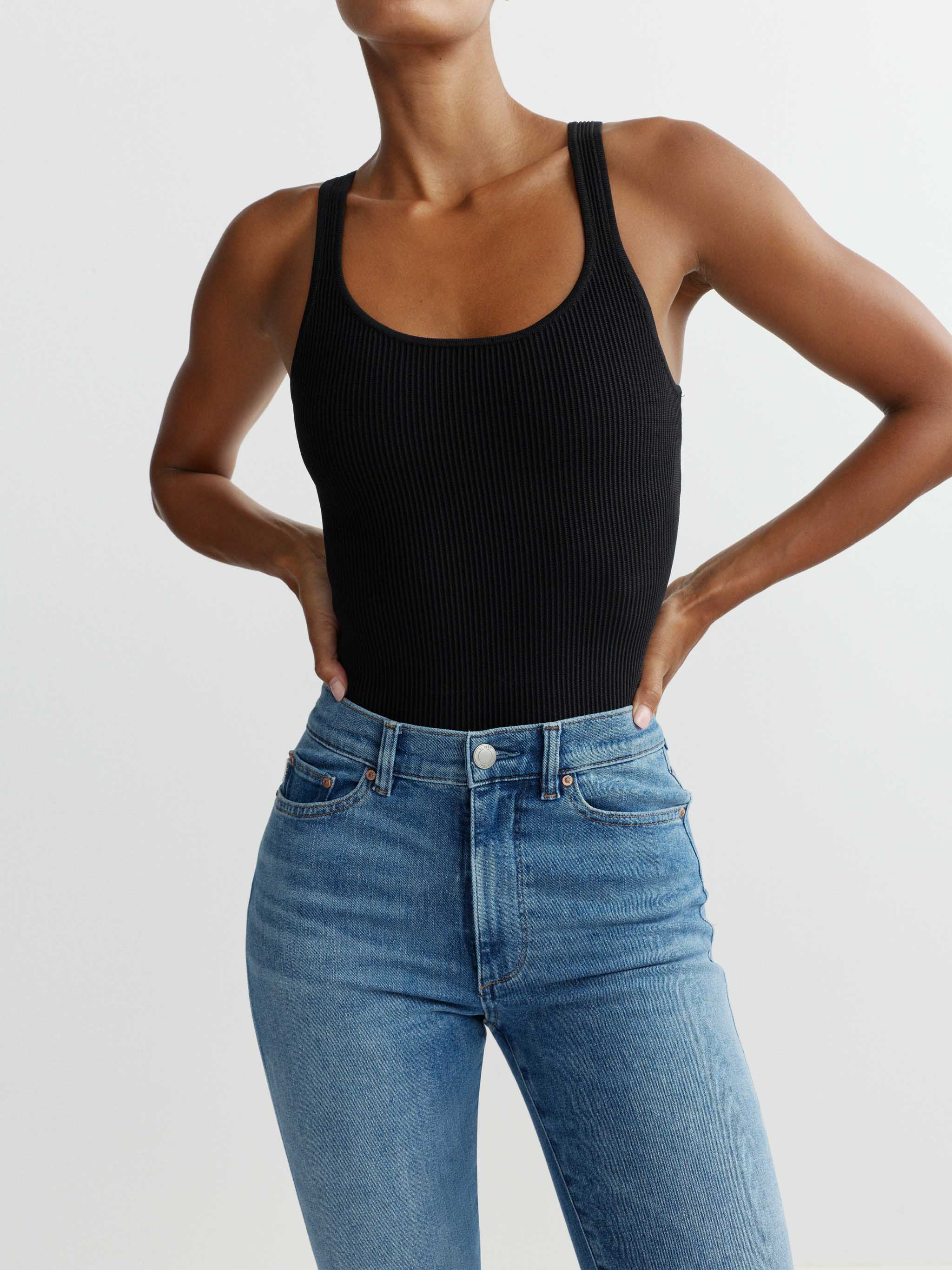 Person wearing a black tank top and blue jeans on a plain background