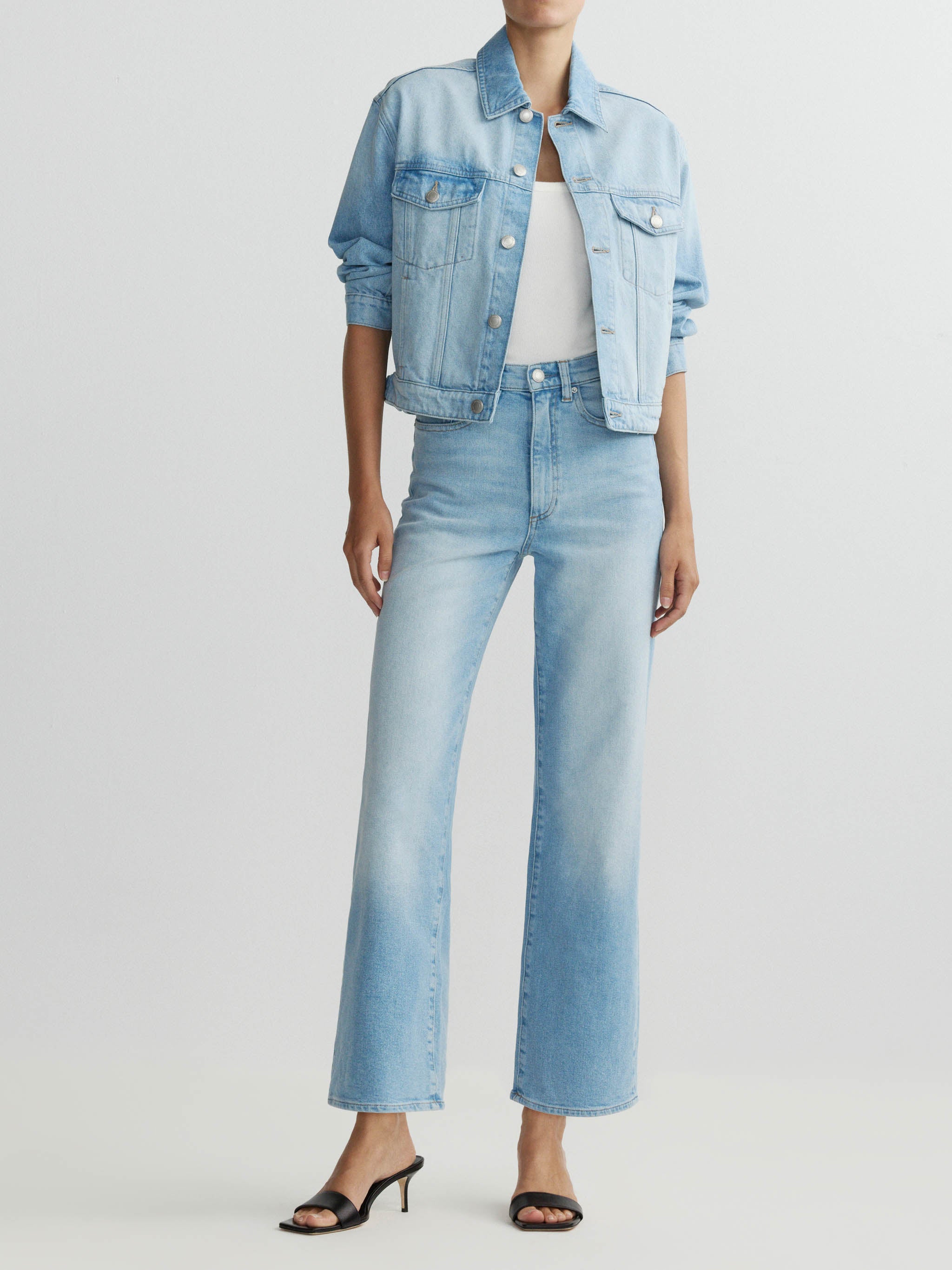 Person wearing a light blue denim jacket and jeans on a white background