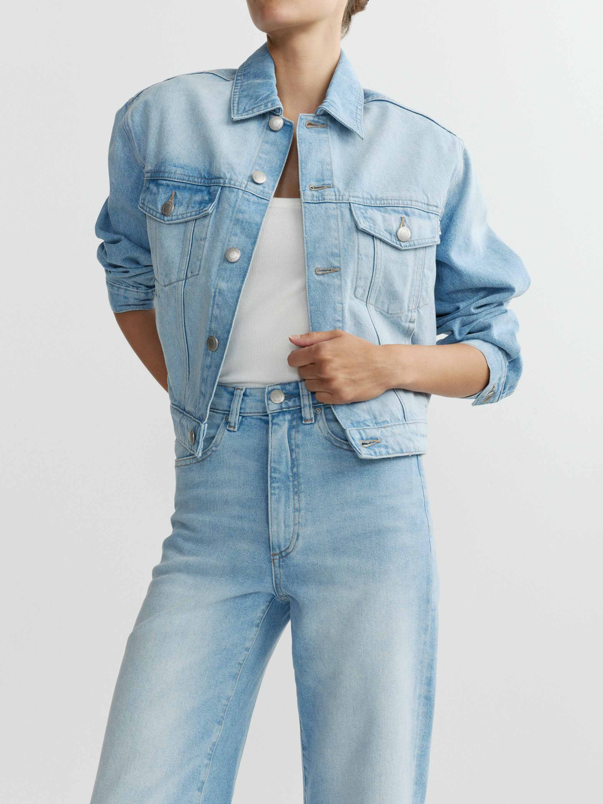 Person wearing a light blue denim jacket and jeans on a plain background