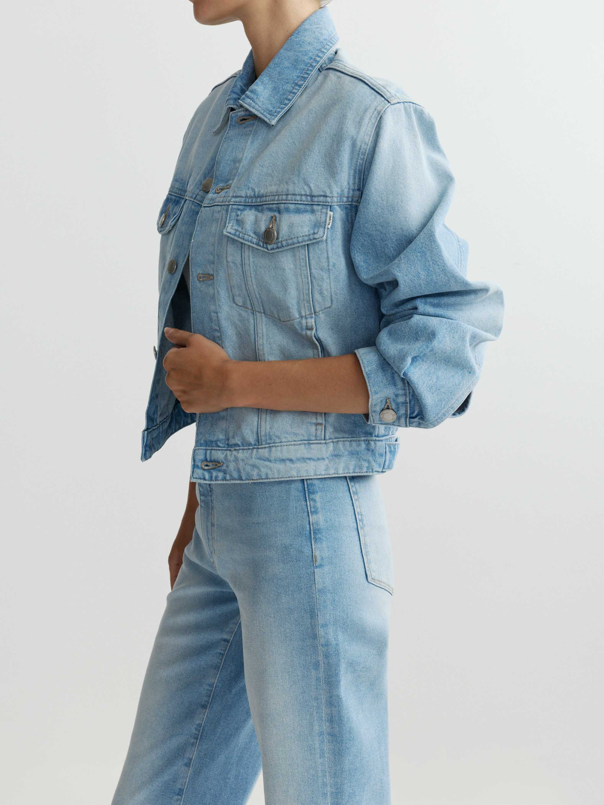 Person wearing a light blue denim jacket and jeans on a white background
