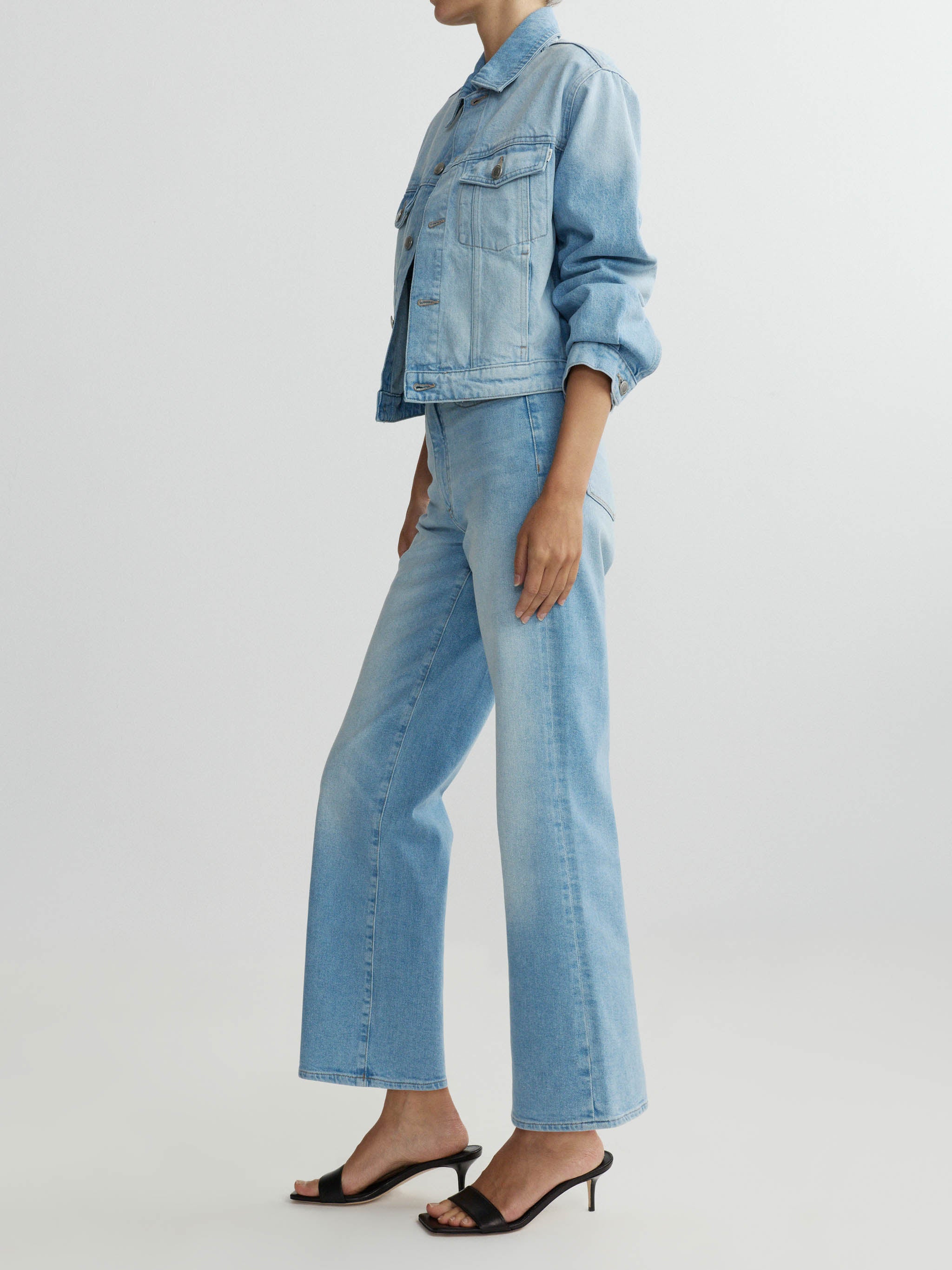 Person wearing a light blue denim jacket and jeans on a white background