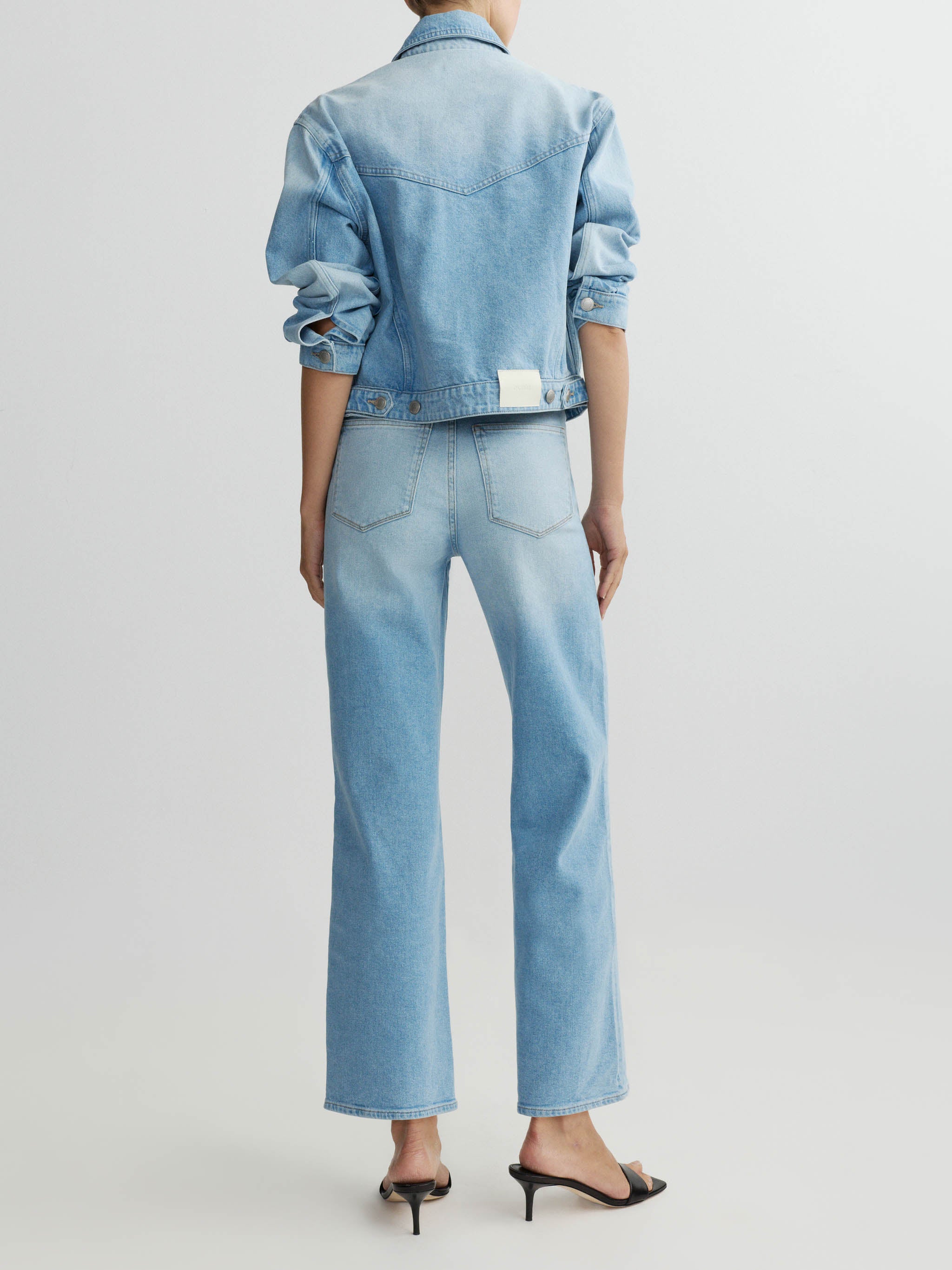 Person wearing a light blue denim jacket and jeans on a white background
