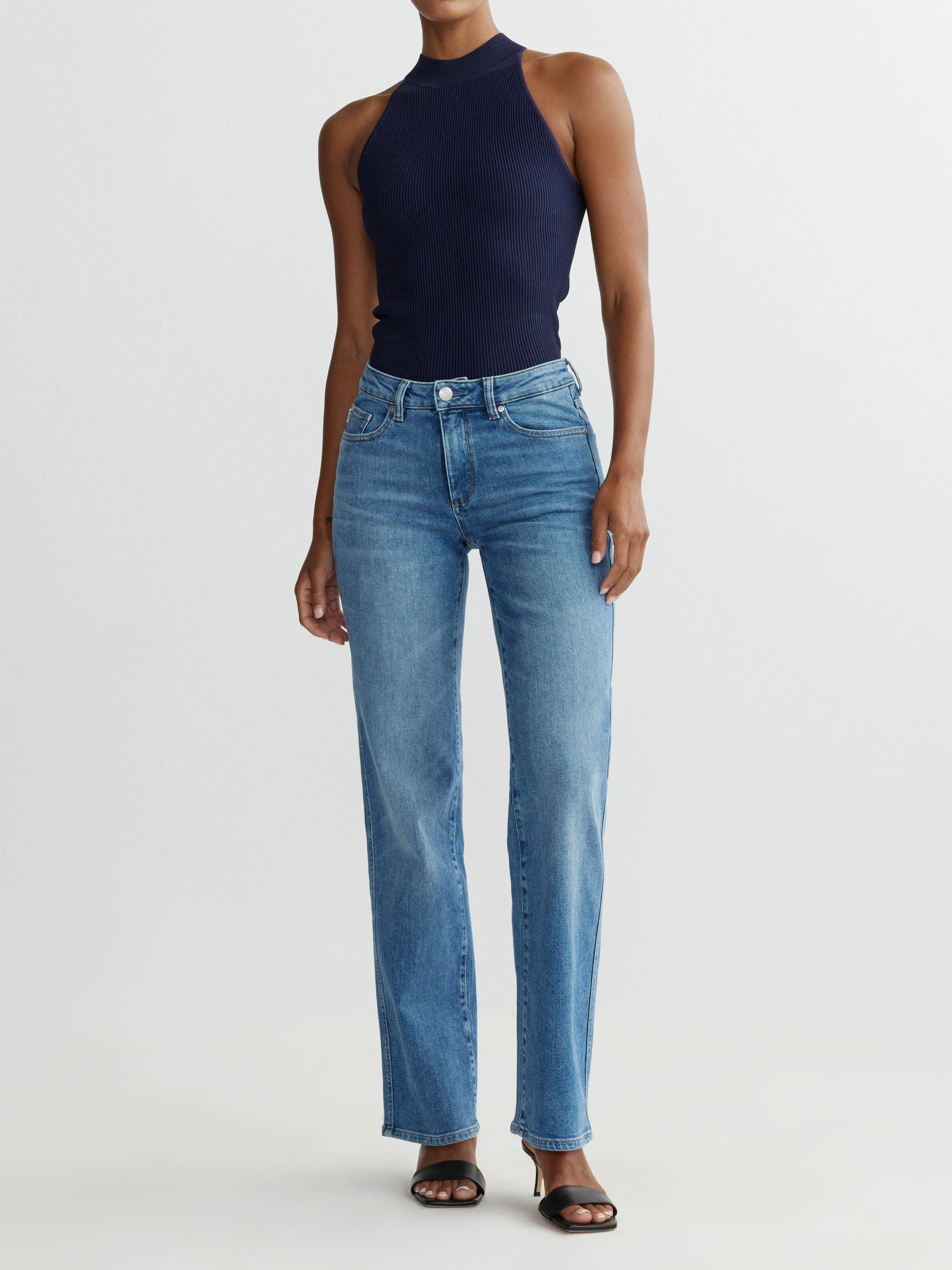 Person wearing a navy halter top and blue jeans on a white background