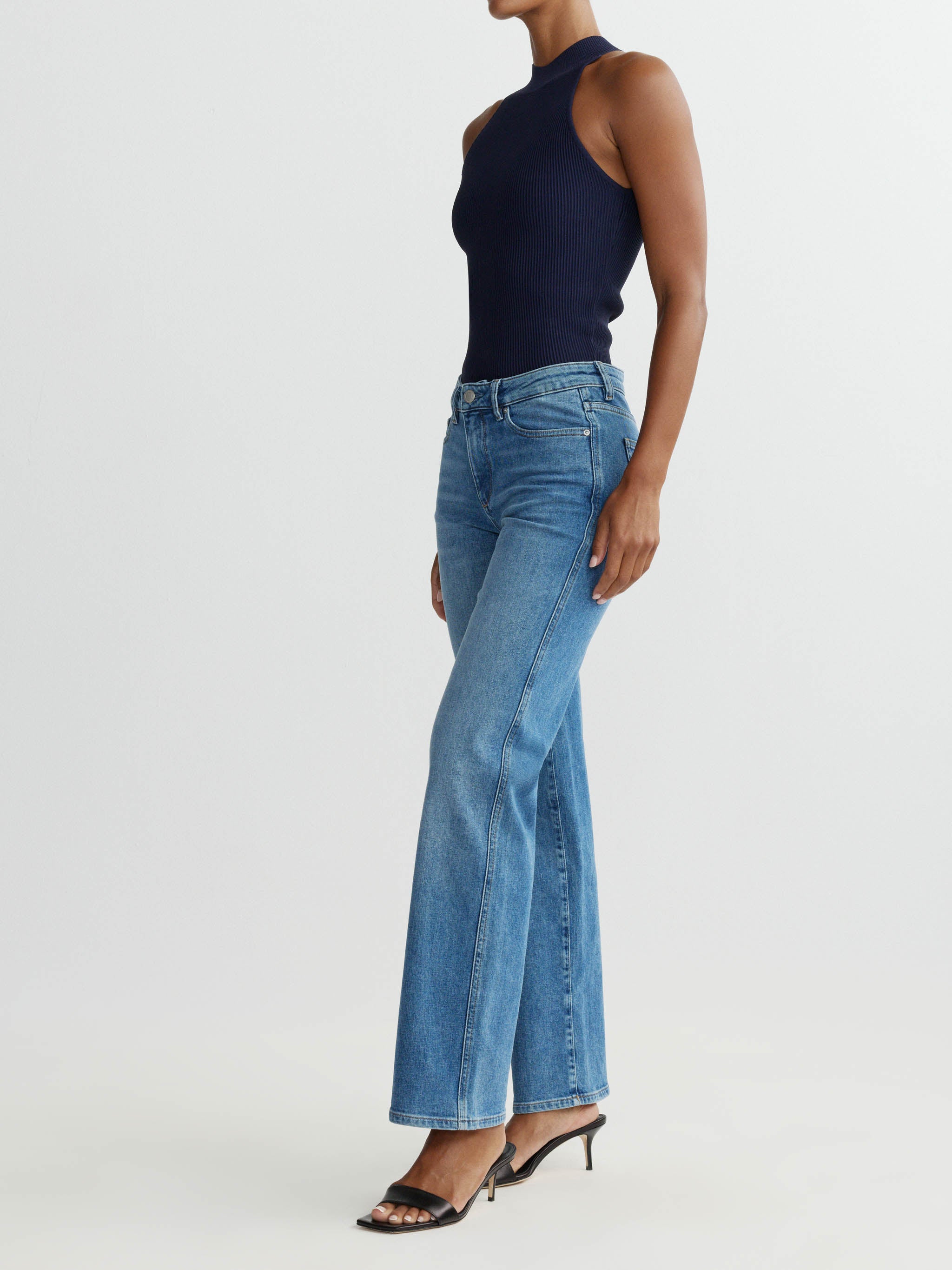 Person wearing blue jeans and a black top on a white background