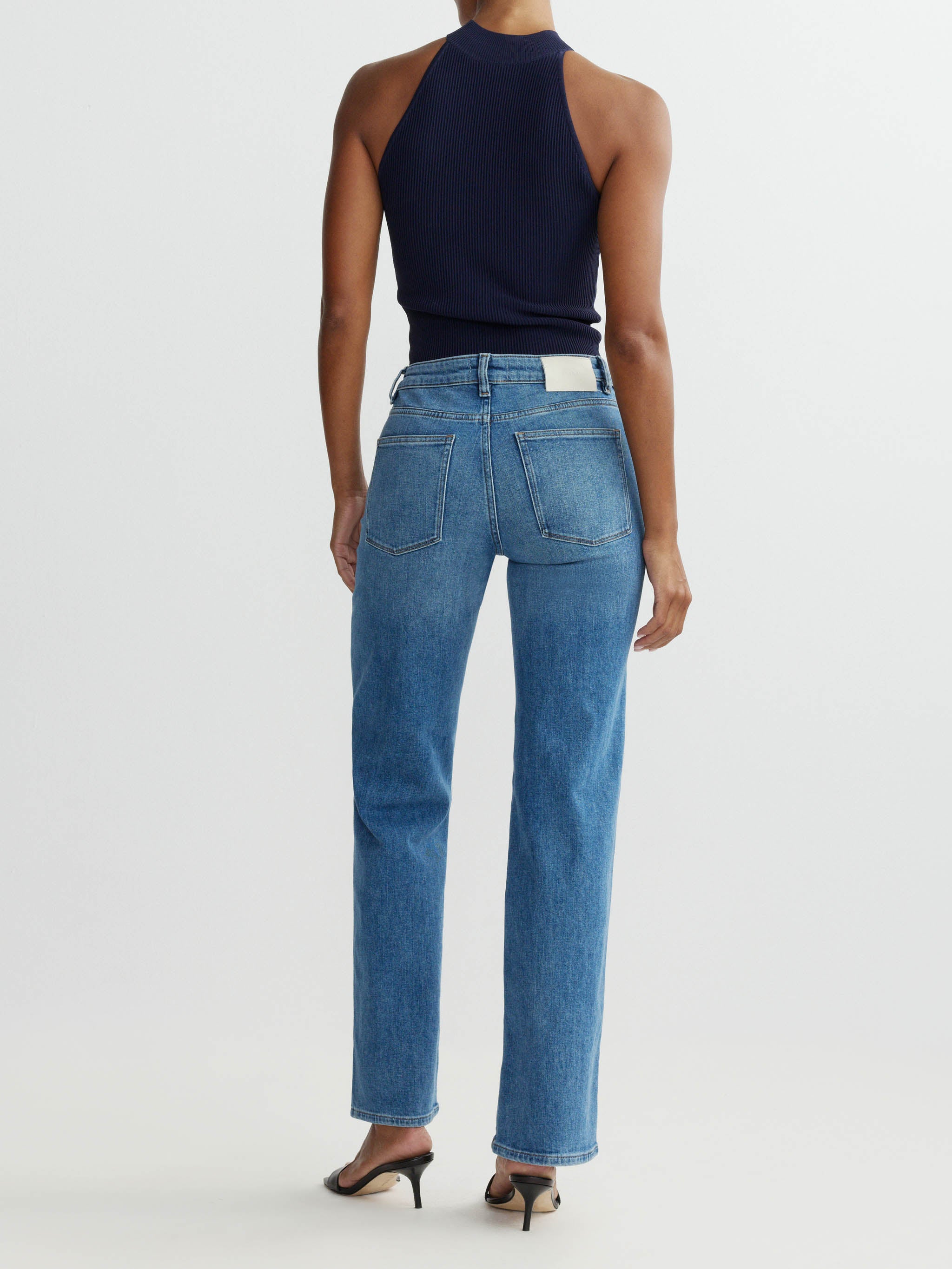 Person wearing blue jeans and a black top on a white background