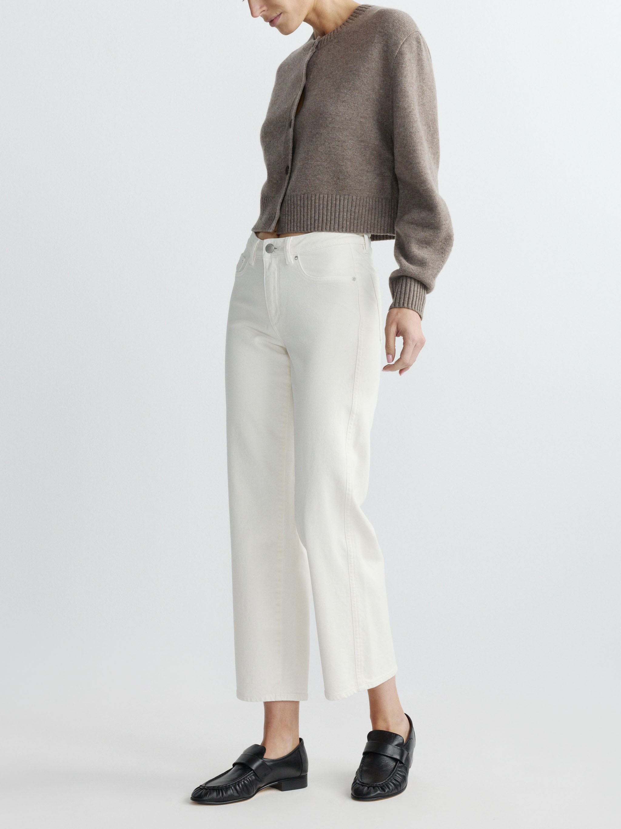Person wearing a brown sweater and white pants on a light gray background