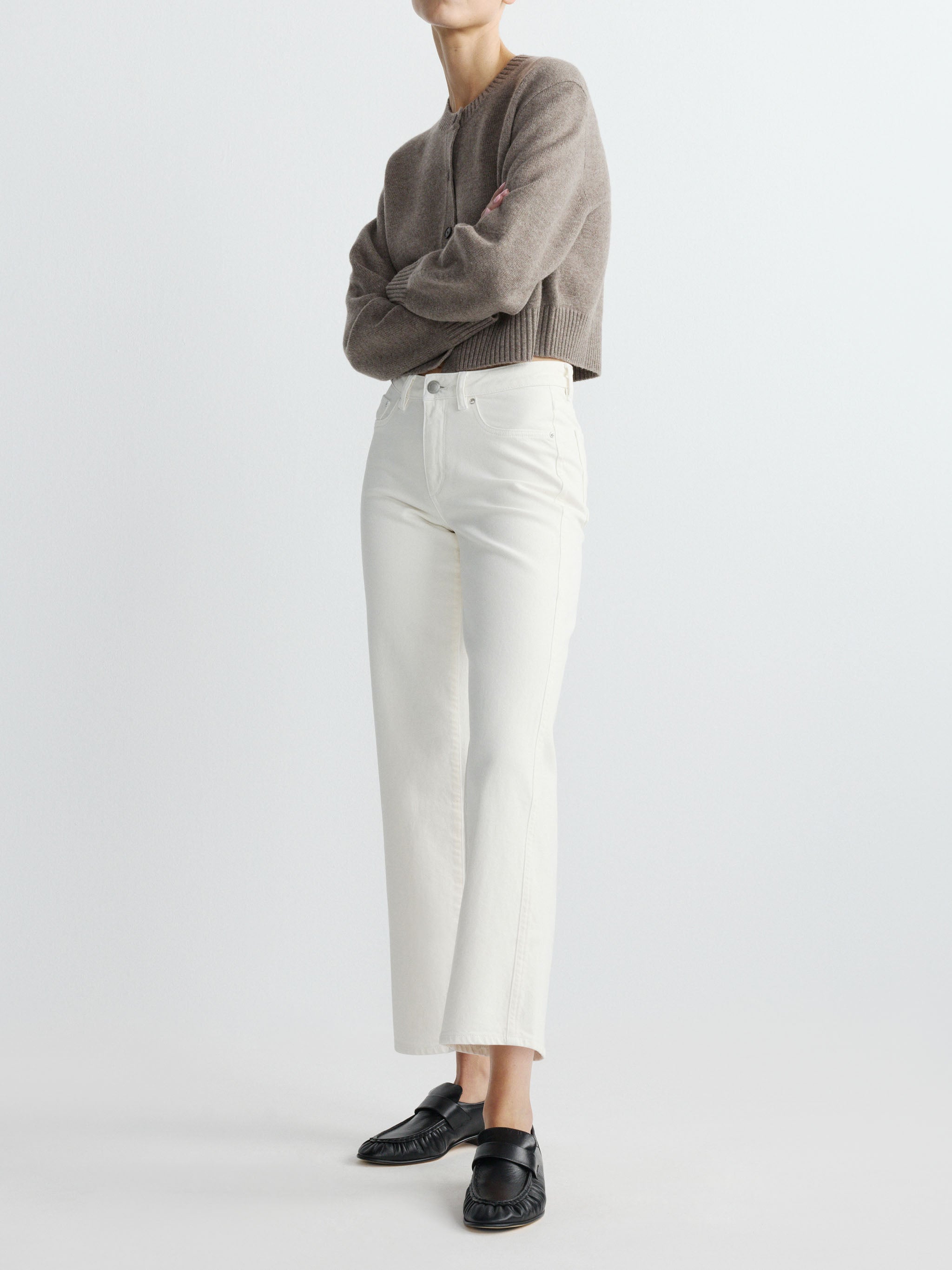 Person wearing a brown sweater and white pants on a plain background