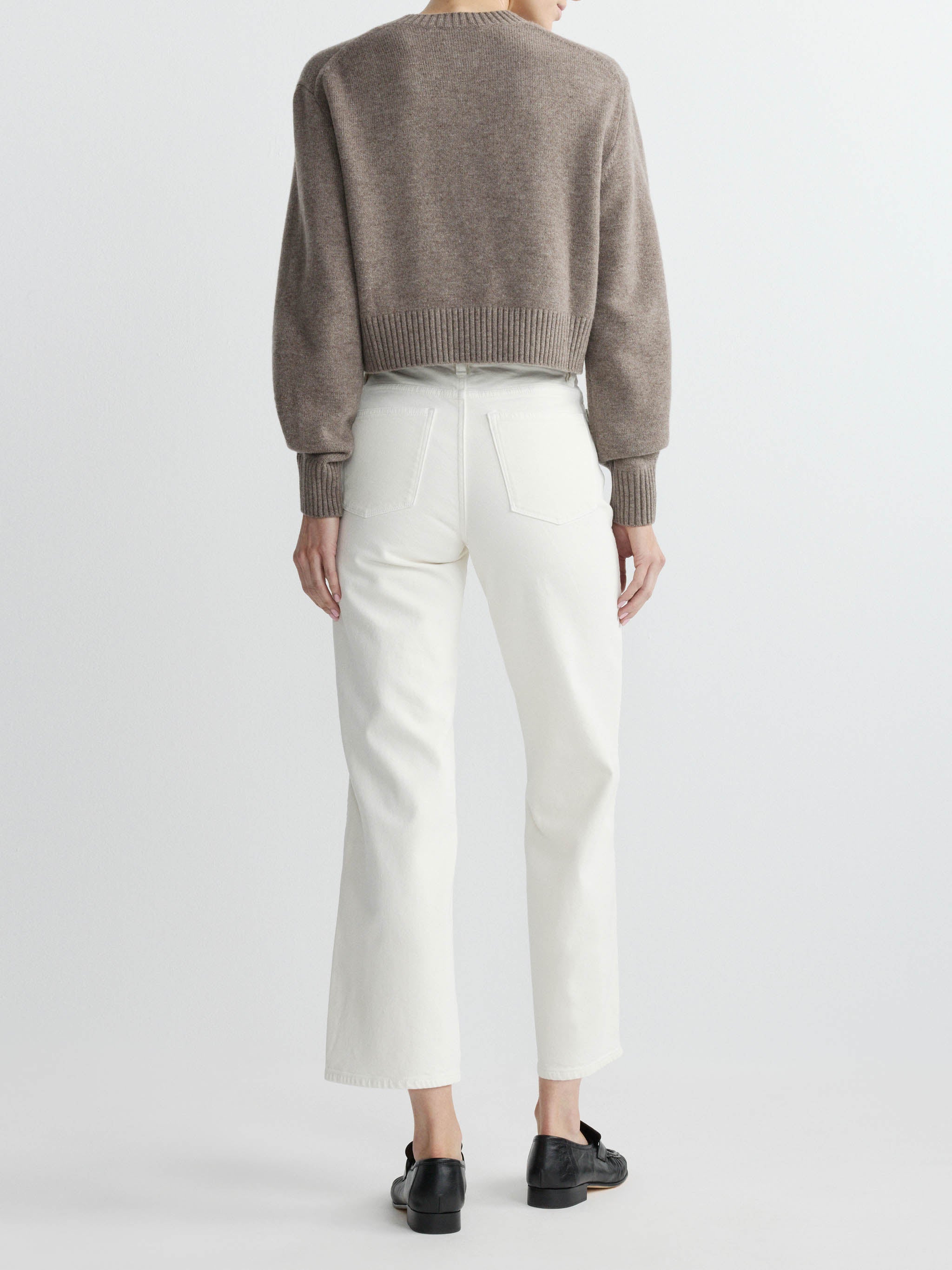 Person wearing a brown sweater and white pants on a light gray background